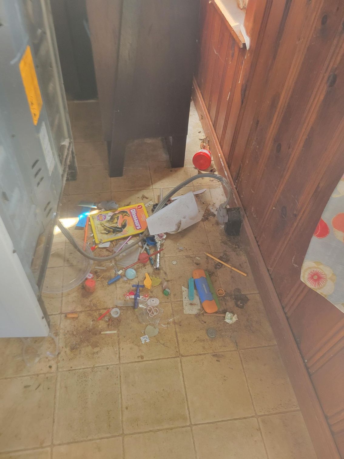 Messy floor with scattered objects; spill stains, near appliance and wood paneling.