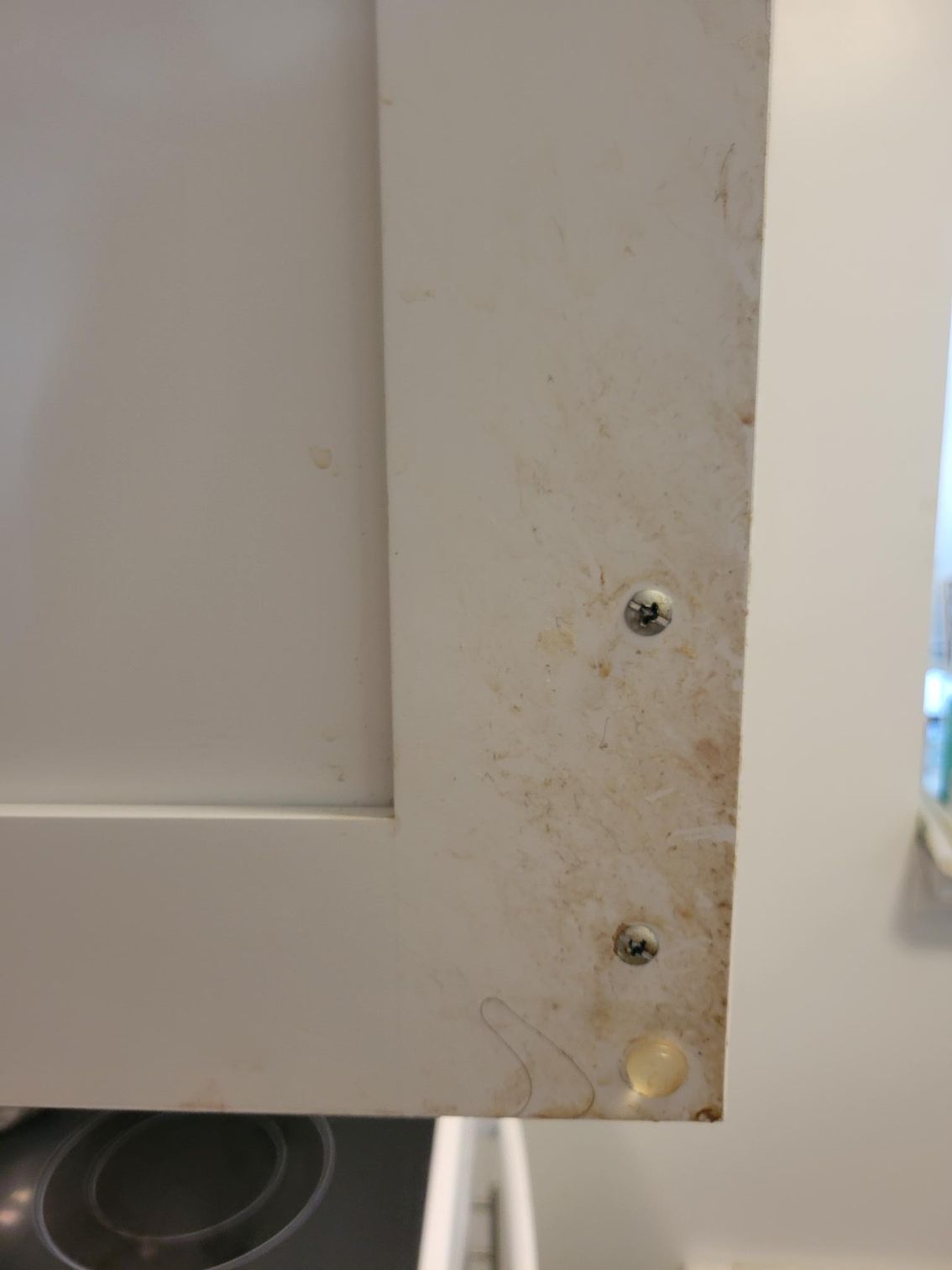White cabinet door corner with visible screws and stains.