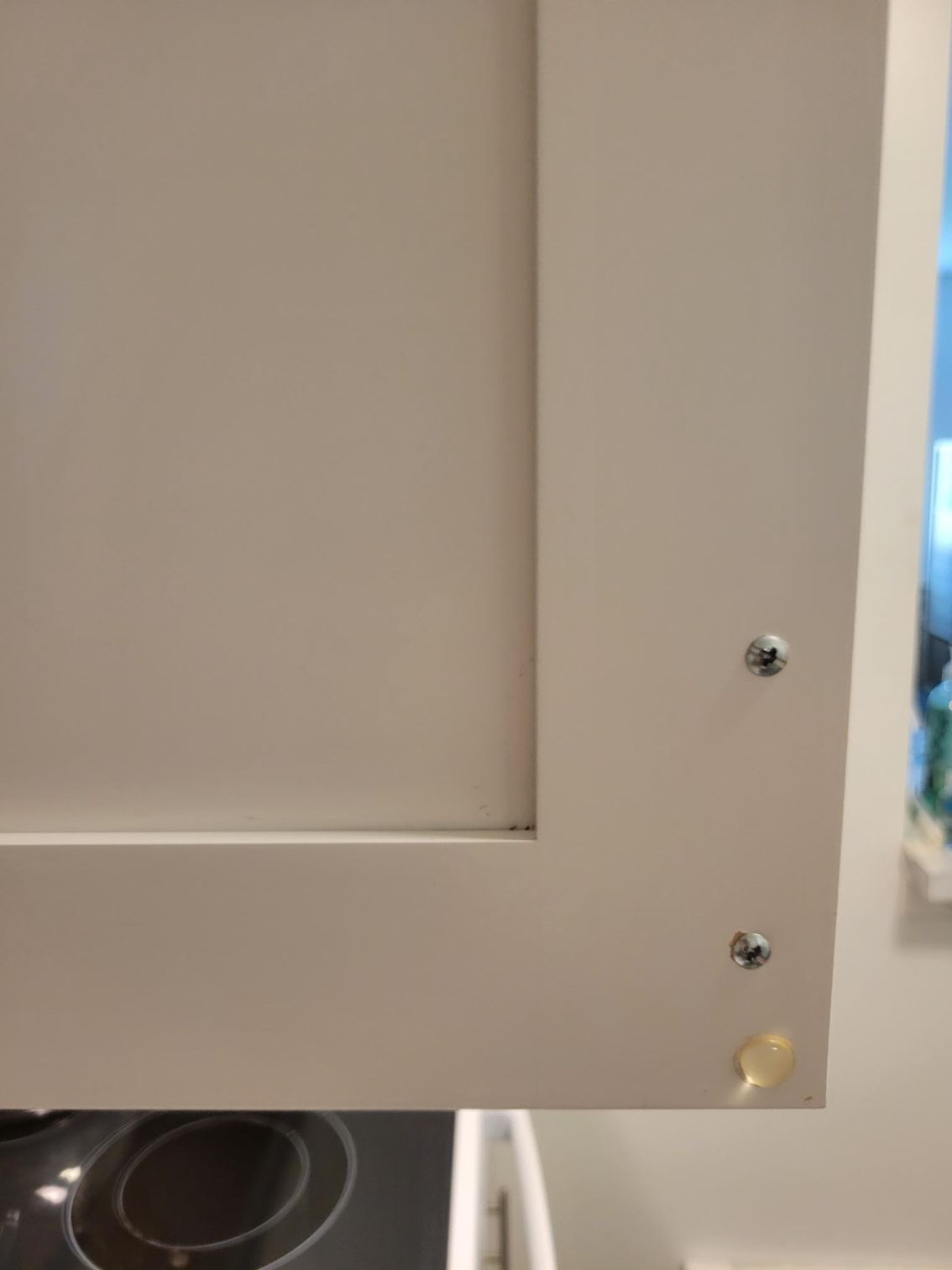Close-up of a white kitchen cabinet door with two screws and a yellow bumper.