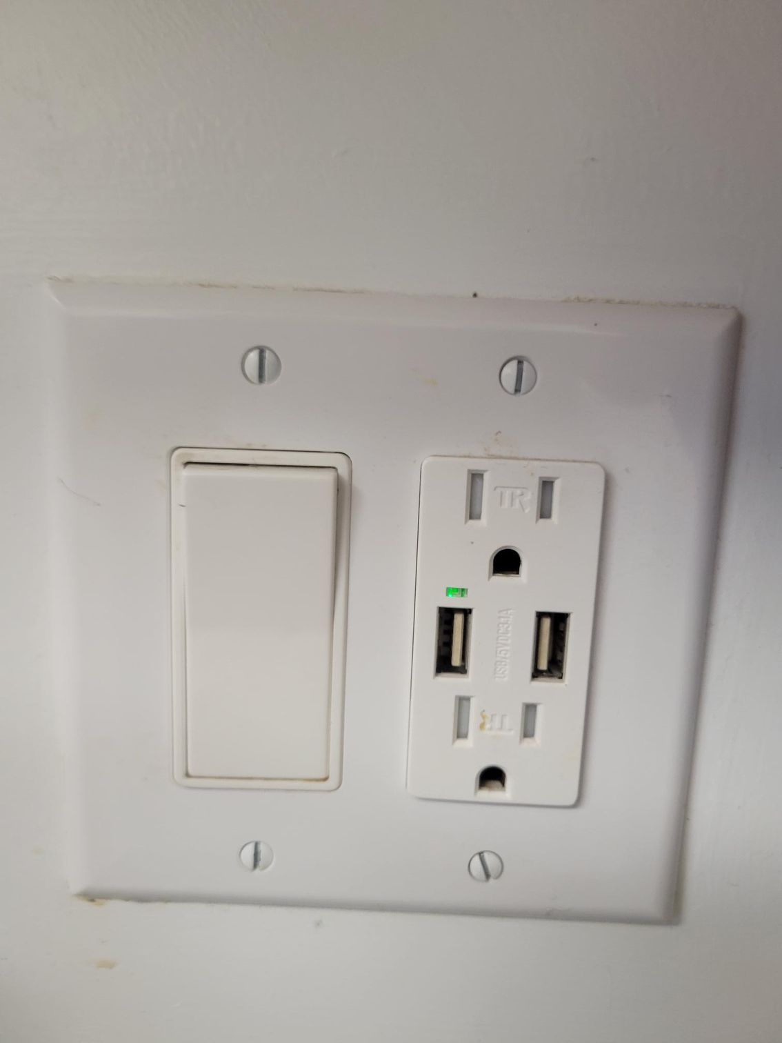 White electrical outlet and light switch on a white wall. The outlet includes USB ports.