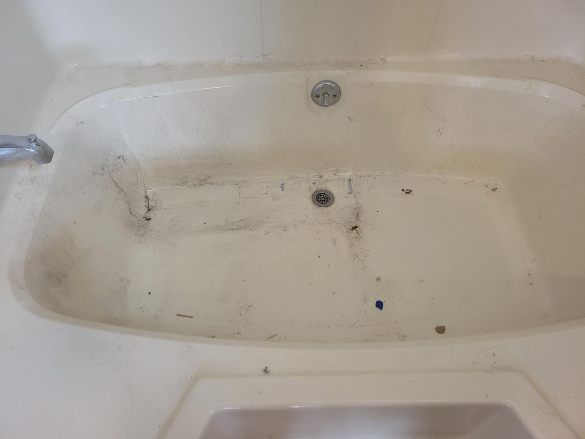 Dirty, off-white bathtub with visible stains and debris. Features drain and faucet in a bathroom setting.