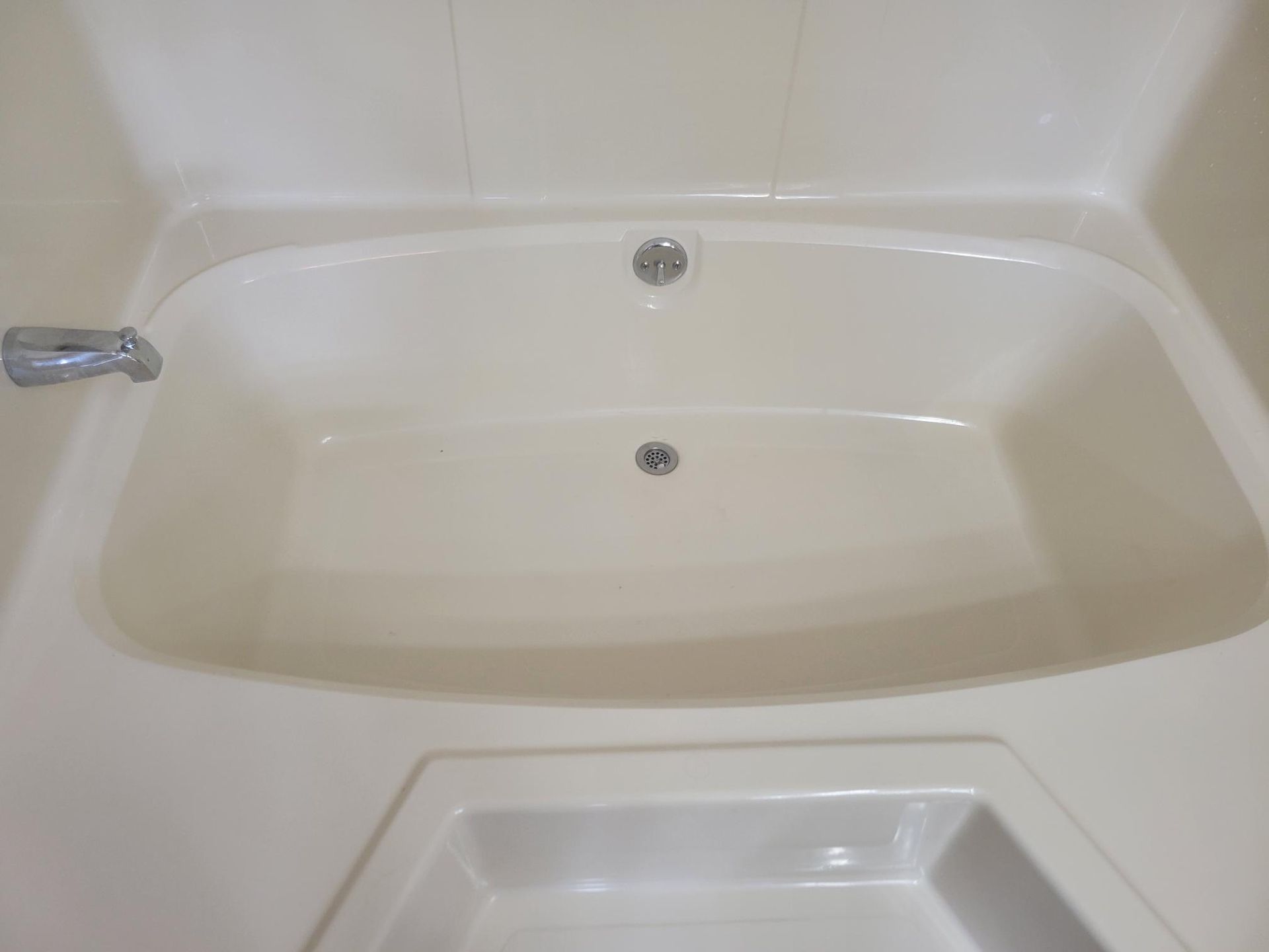 Cream-colored bathtub with two drains and a faucet, set within white walls, with a lower shelf.