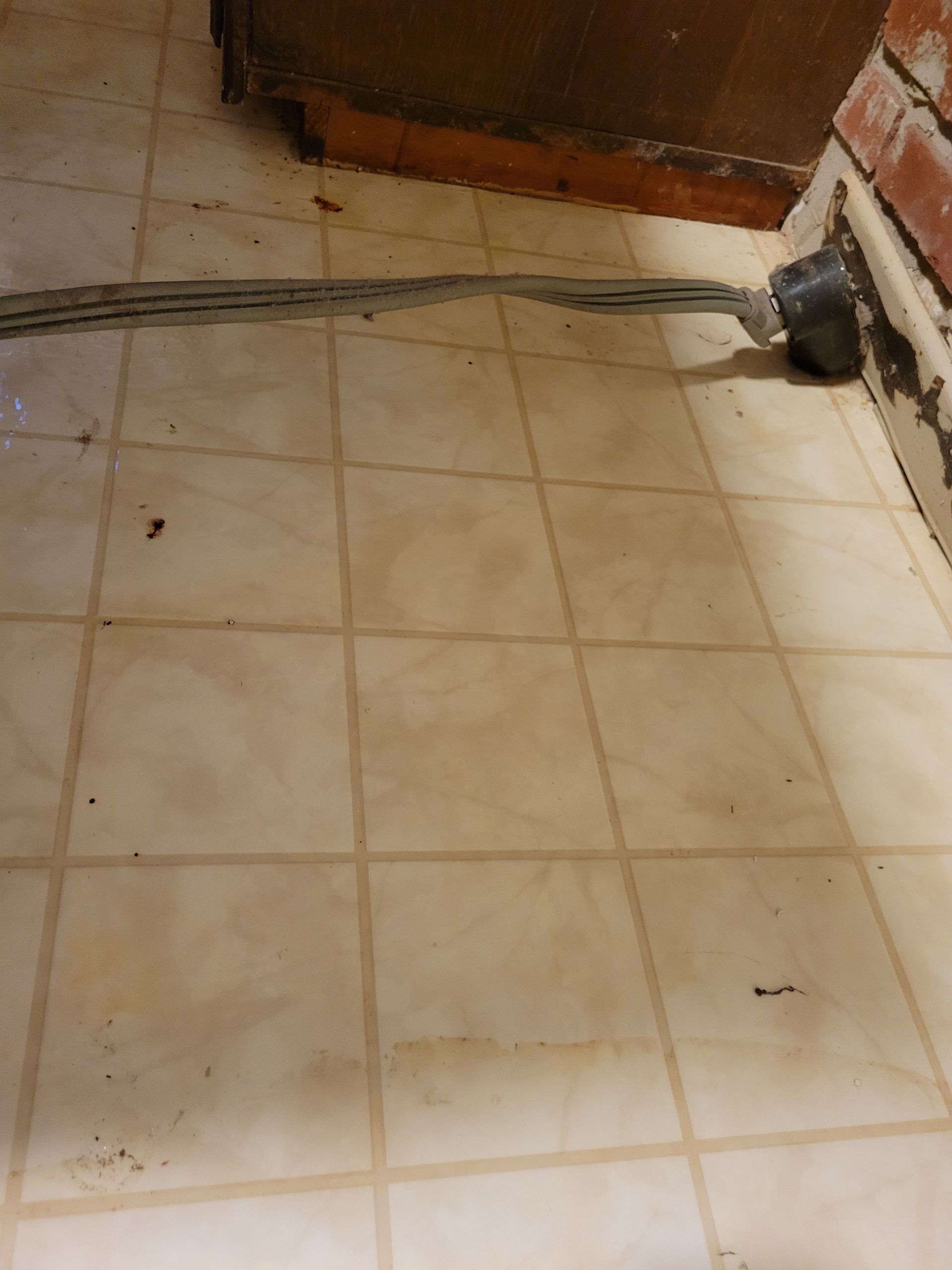 Beige tile floor with a gray seam, a pipe, and a brick wall.