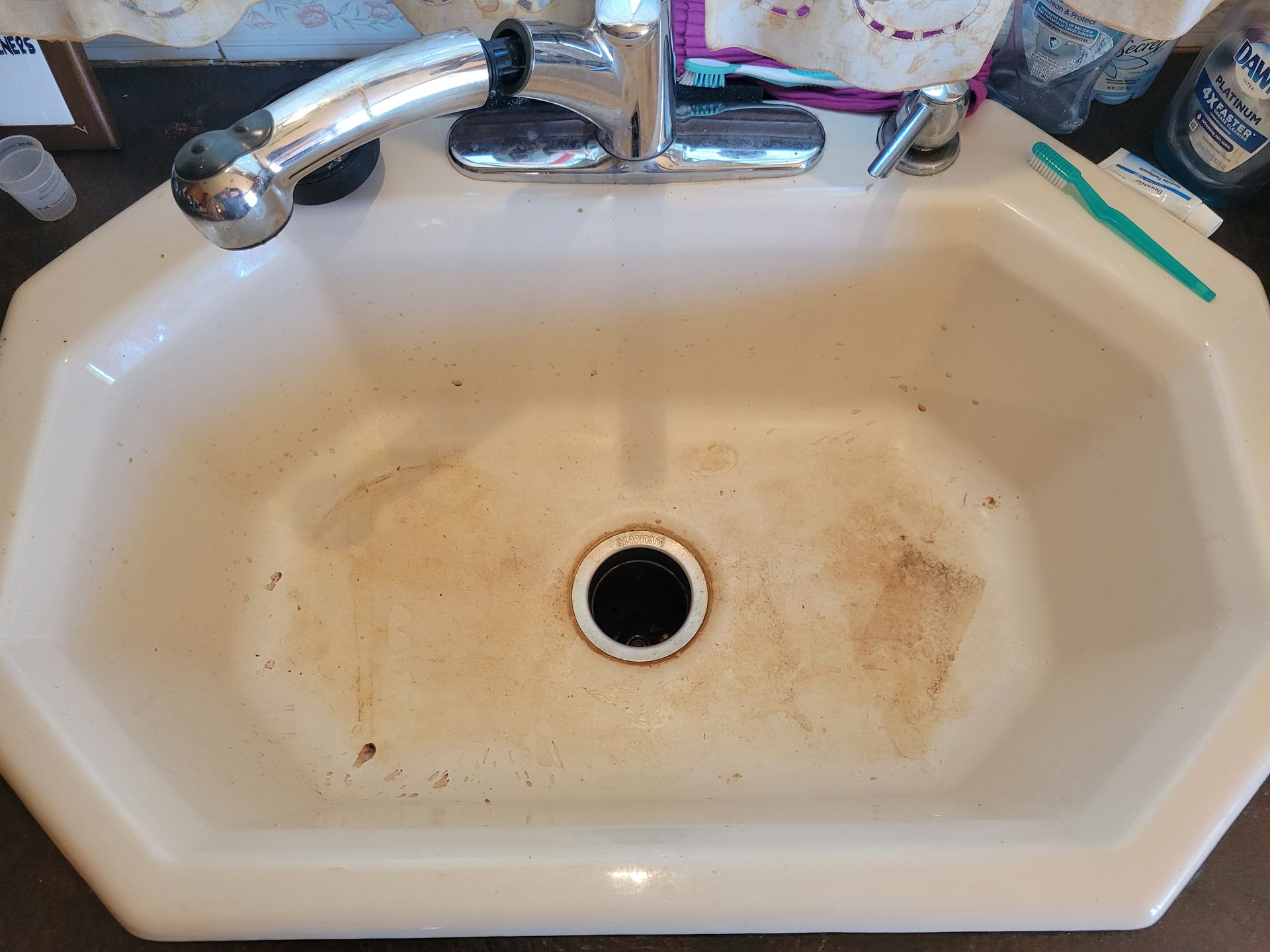 Dirty, off-white, octagonal bathroom sink with chrome faucet. Brown stains and debris visible inside the basin.