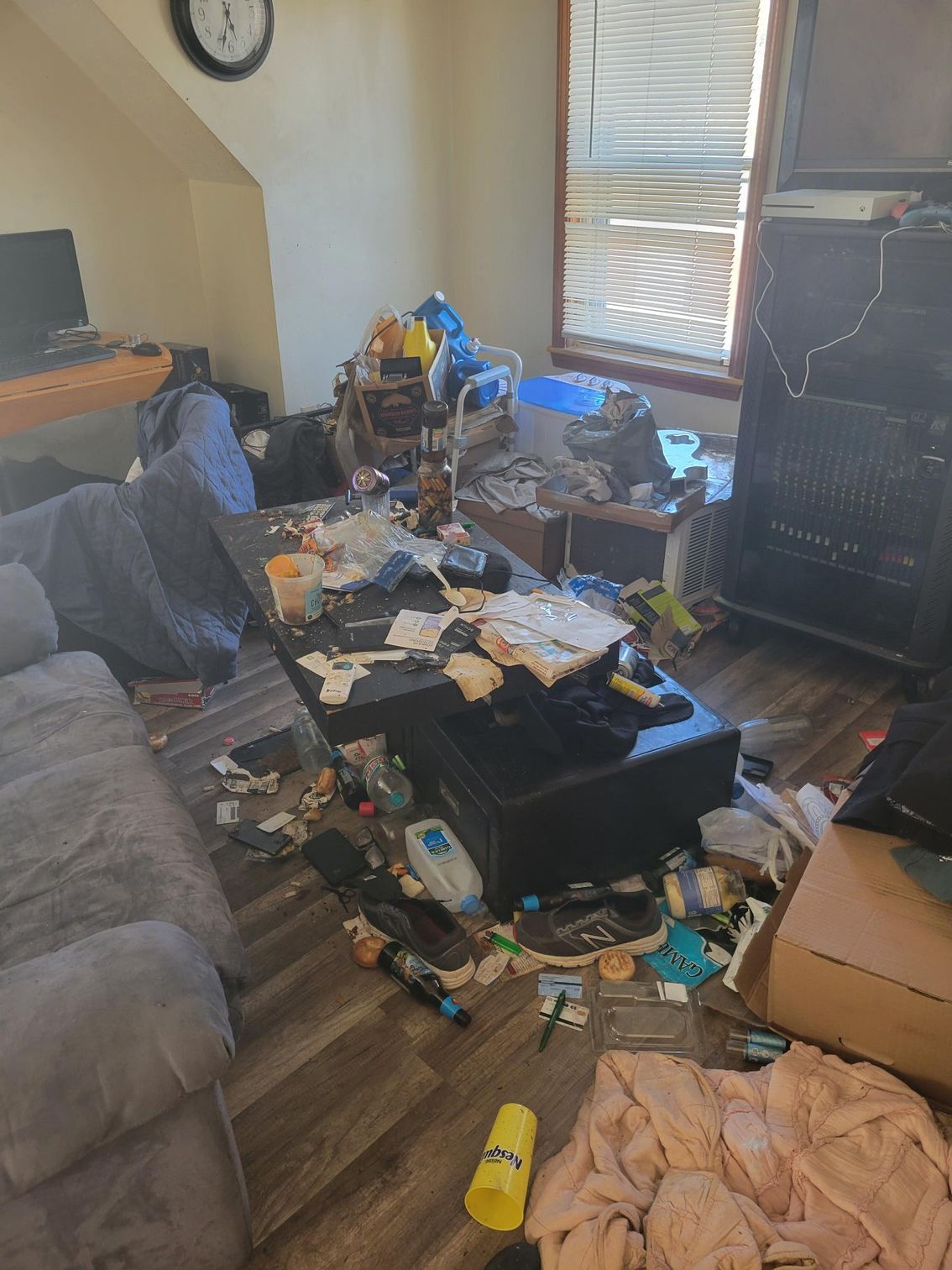 Messy living room with trash and clutter covering floors and furniture.