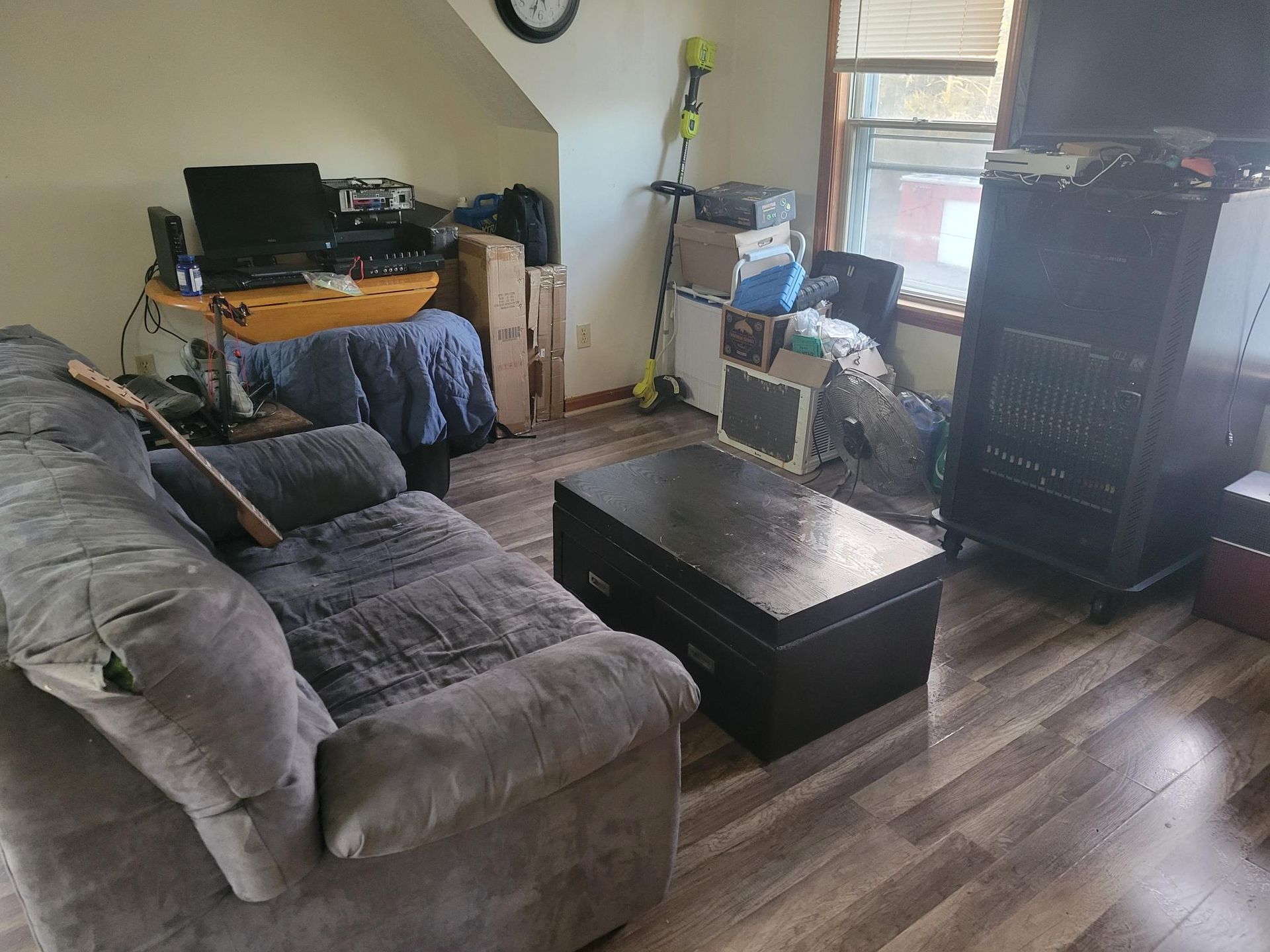Living room with gray couch, dark coffee table, cluttered desk, and window.