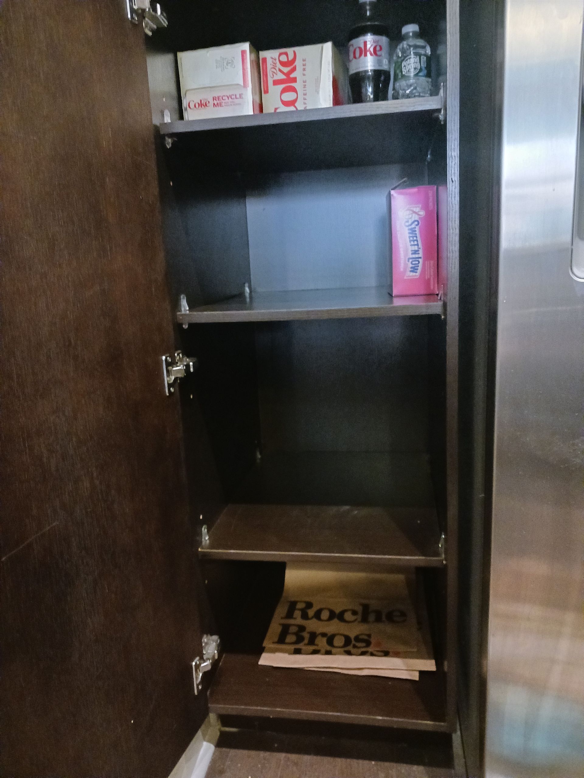 A pantry with shelves holding snacks, drinks, and a grocery store sign; the door is open.
