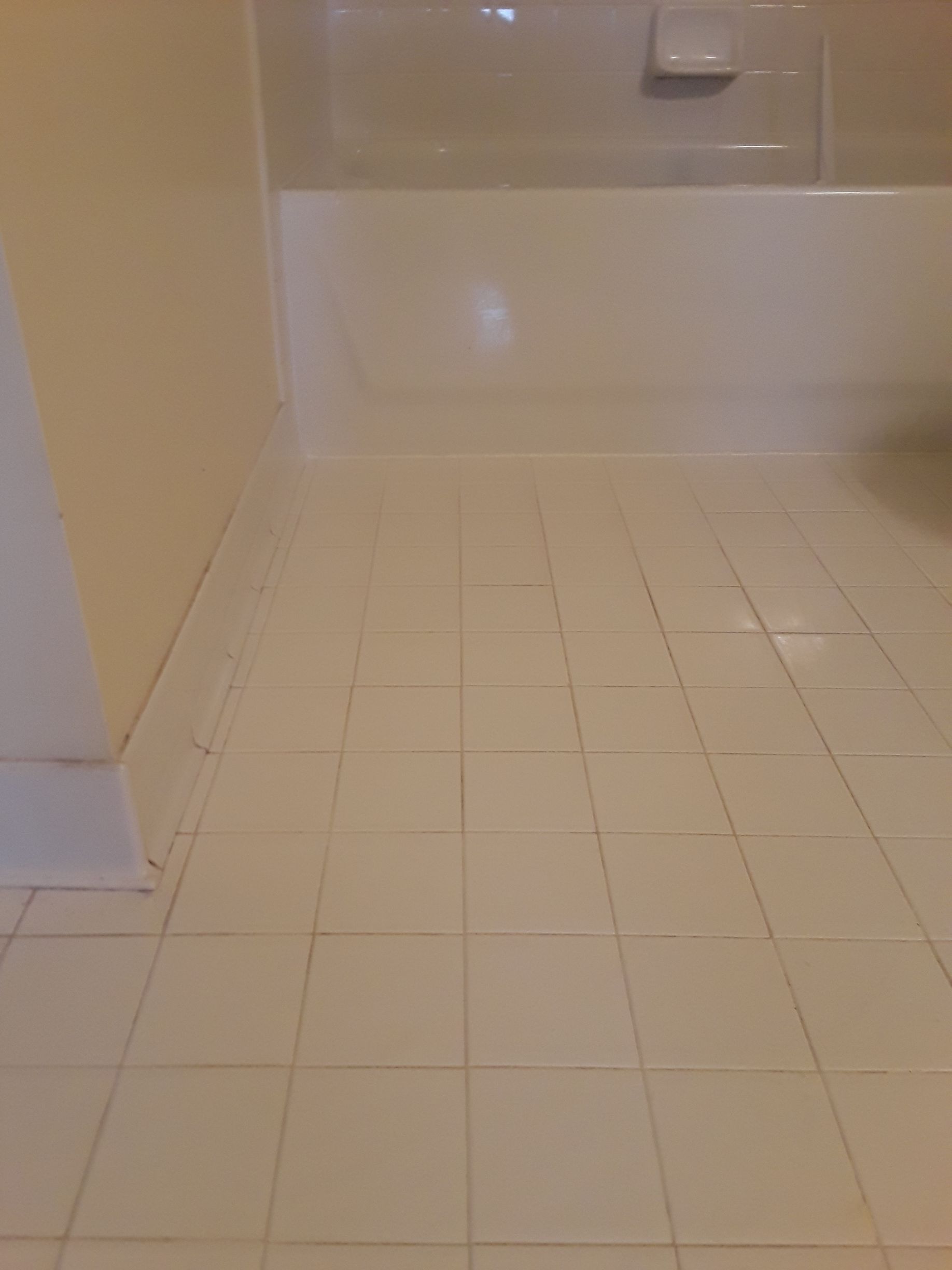 Bathroom floor with white tile and beige walls leading to a bathtub.
