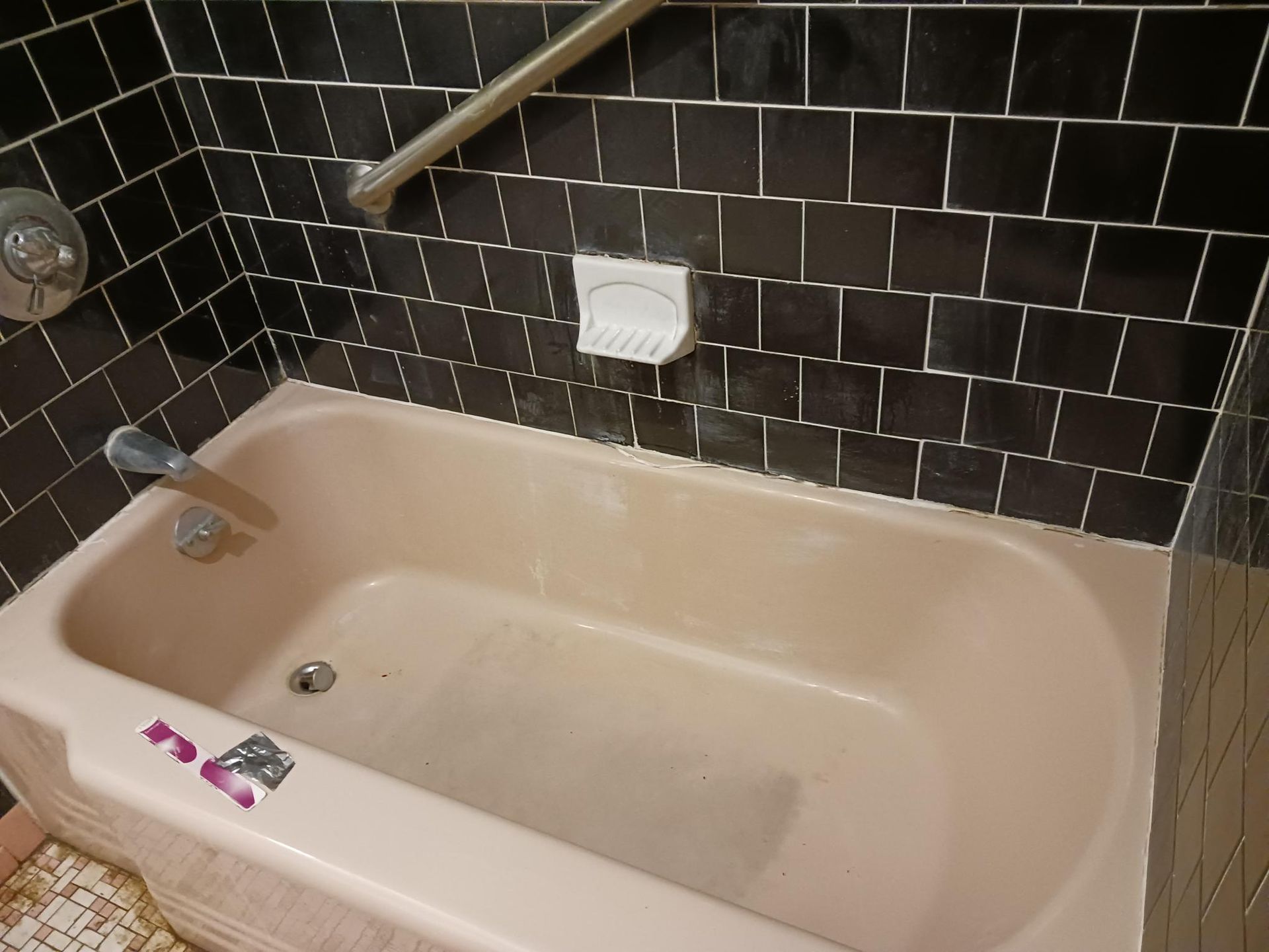 Pink bathtub with black tiled wall, soap dish, and grab bar.
