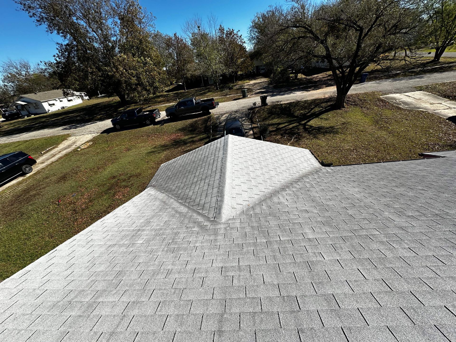 View from a roof looking down at gray shingles and a street with cars and houses on a sunny day.