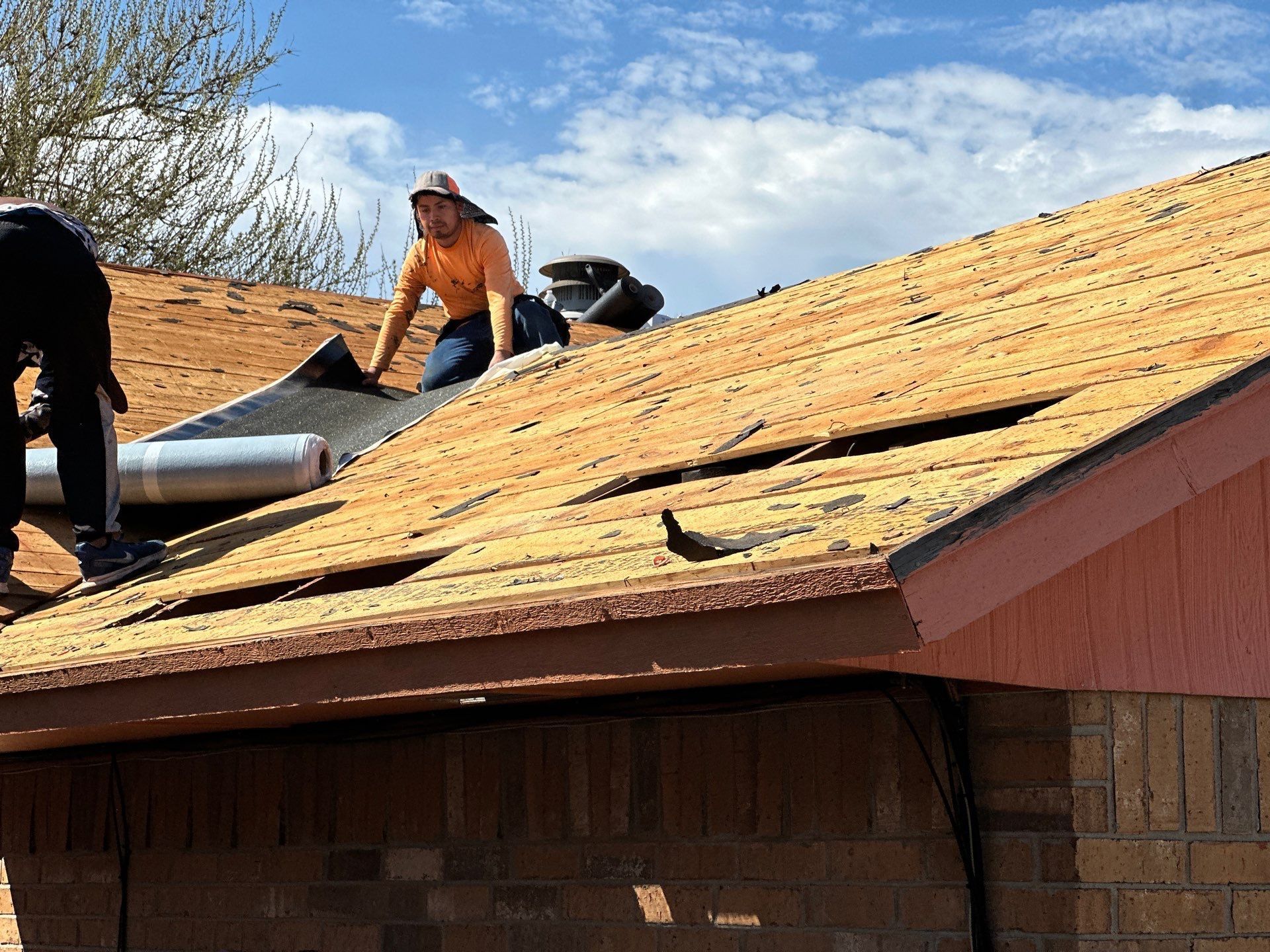 Two roofers are working on a roof, removing old shingles. 