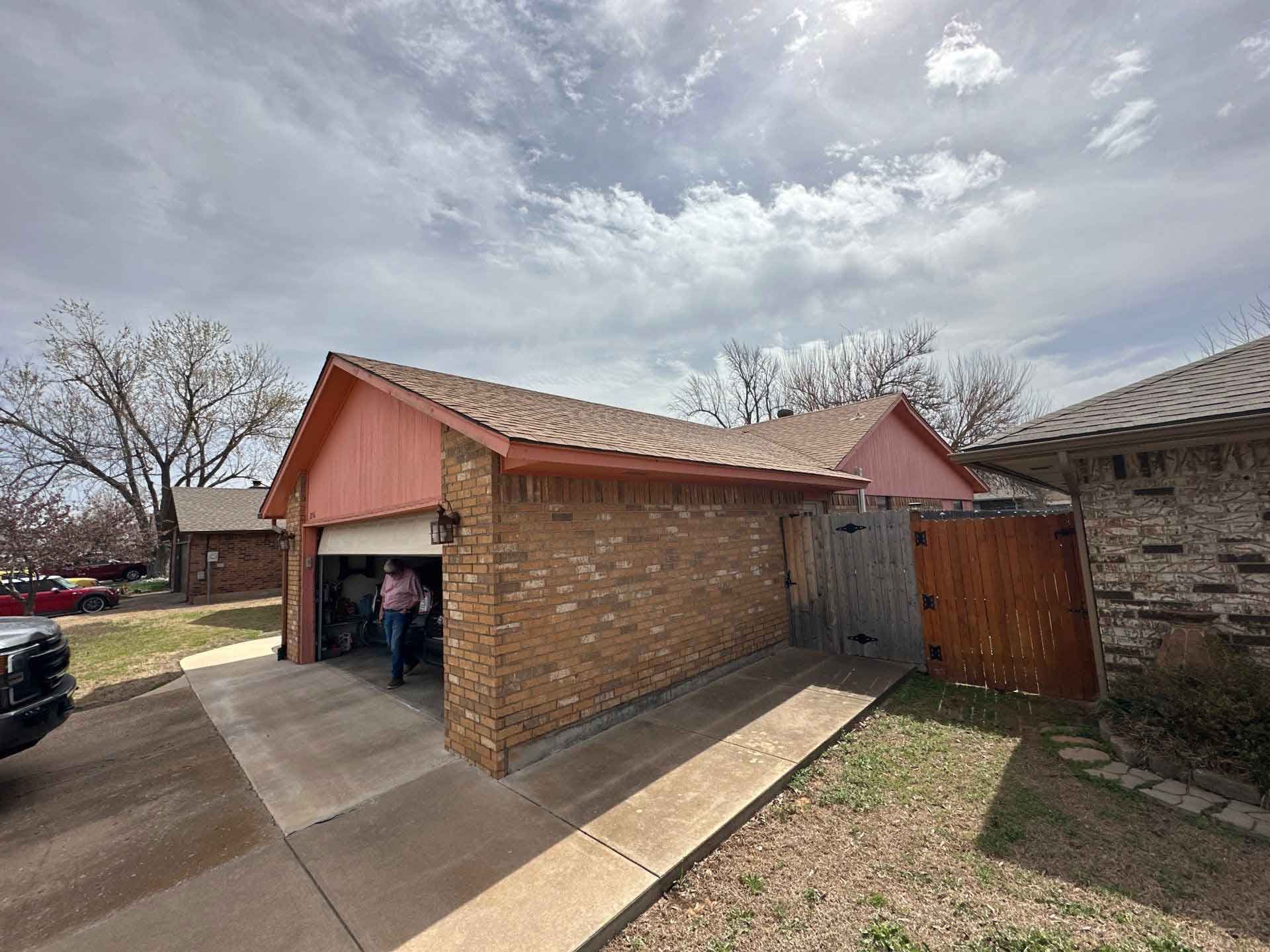 A man is standing in a garage next to a brick house.