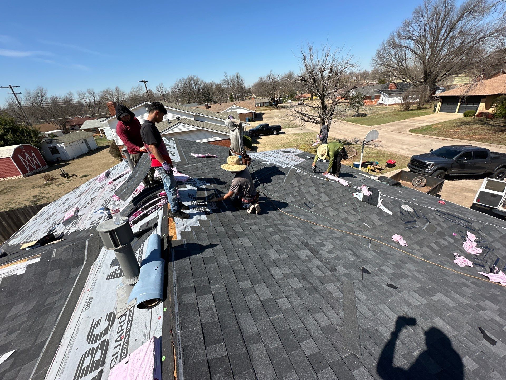 People installing shingles on a rooftop. Sunlight and blue sky. Others on the roof are inspecting.