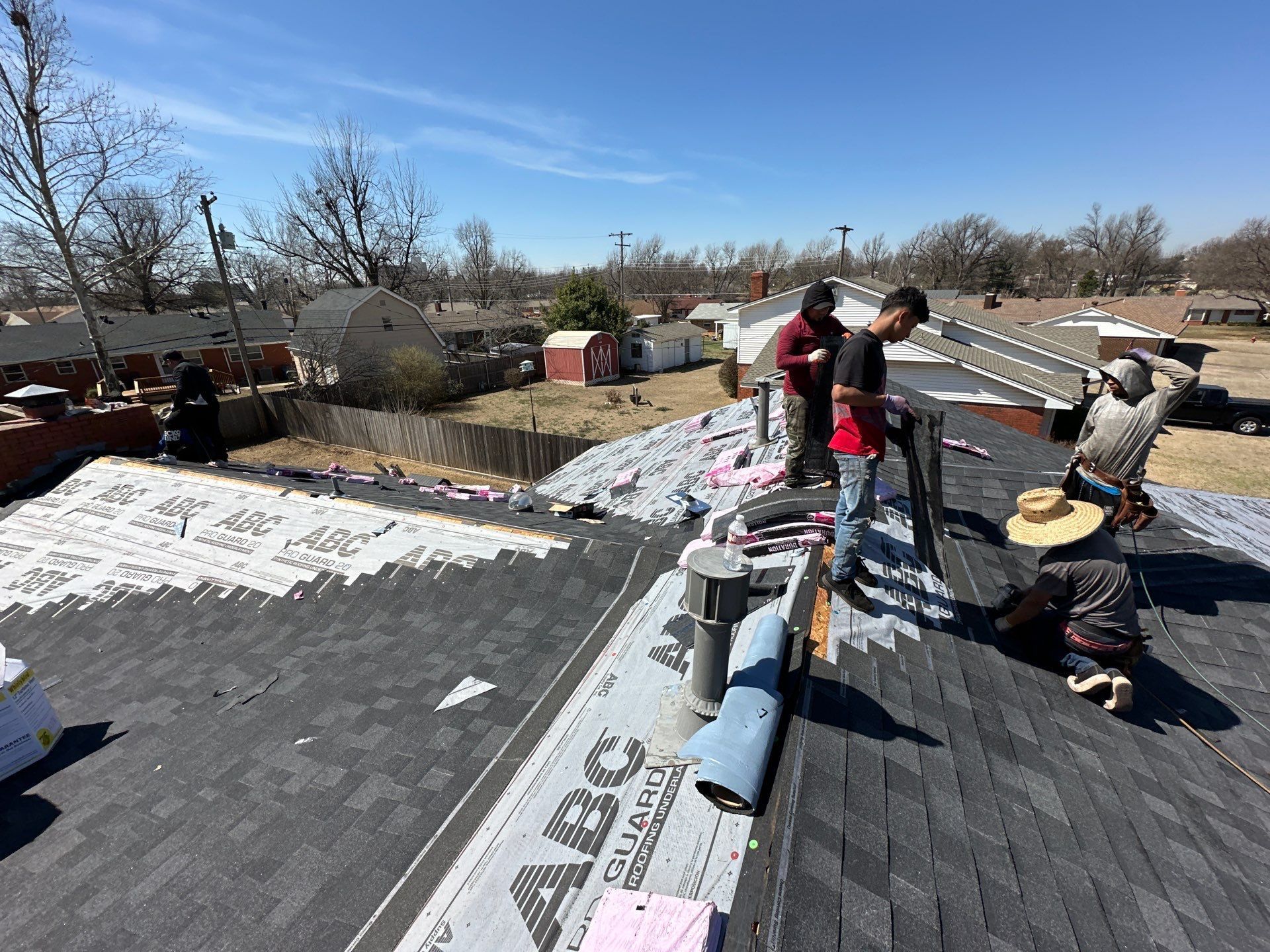 Roofers installing shingles on a sunny day. They are working on the roof of a house in a residential neighborhood.
