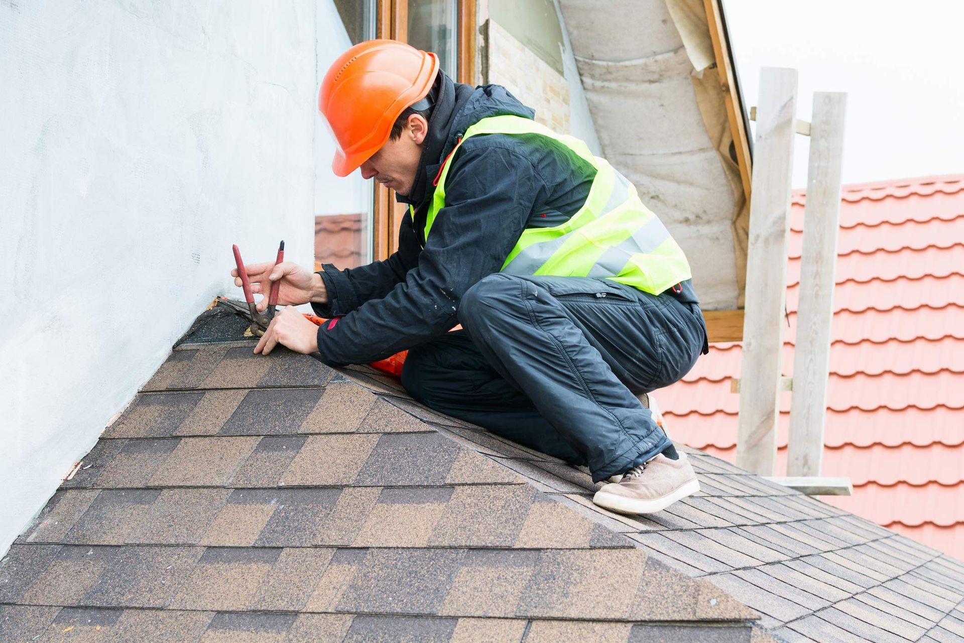 A roofing service contractor wearing protective gear is dismantling old roof shingles. A roofing service contractor wearing protective gear is dismantling old roof shingles.