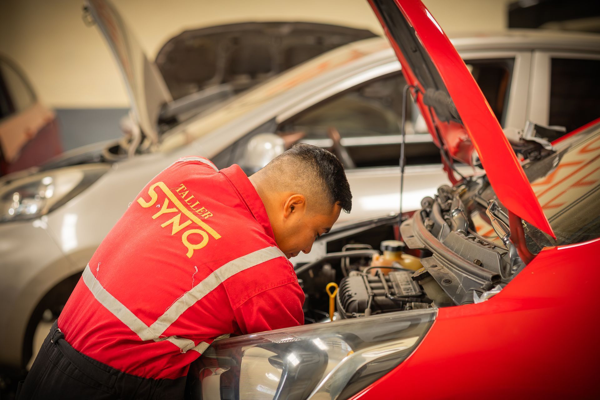 Un hombre está trabajando bajo el capó de un coche rojo.