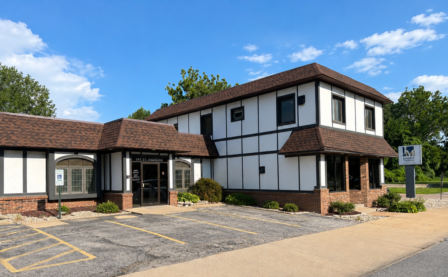 Two-story office building with white walls, brown roof, and a paved parking lot under a blue sky