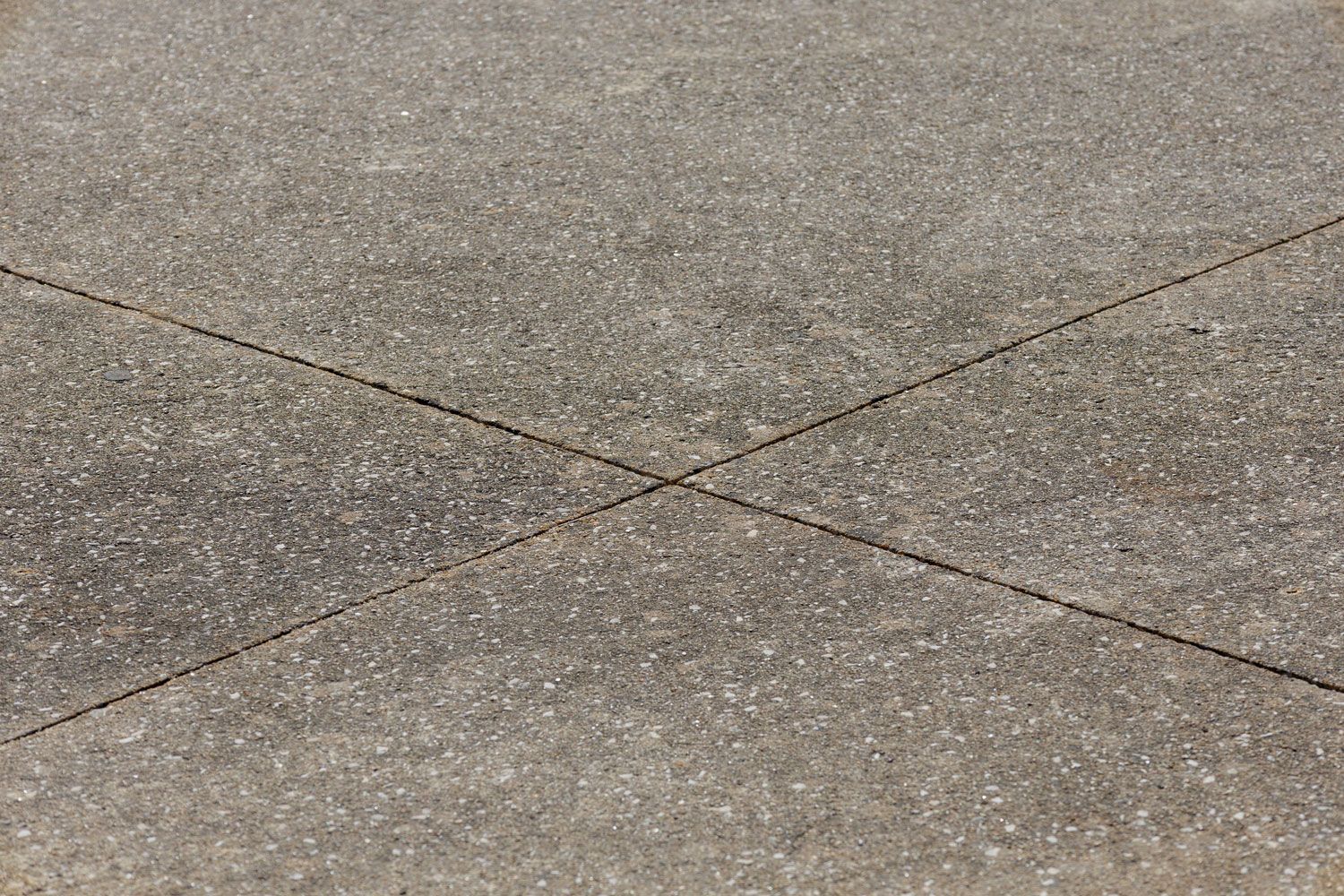 Close-up of a textured concrete surface with intersecting seam lines forming an X.