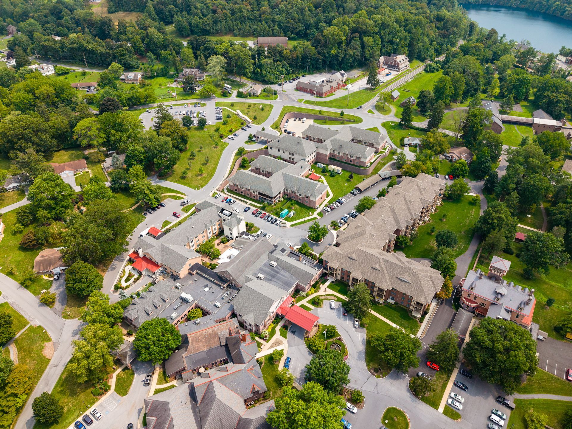 Aerial view of a lakeside campus with gray-roofed buildings, trees, roads, and parked cars