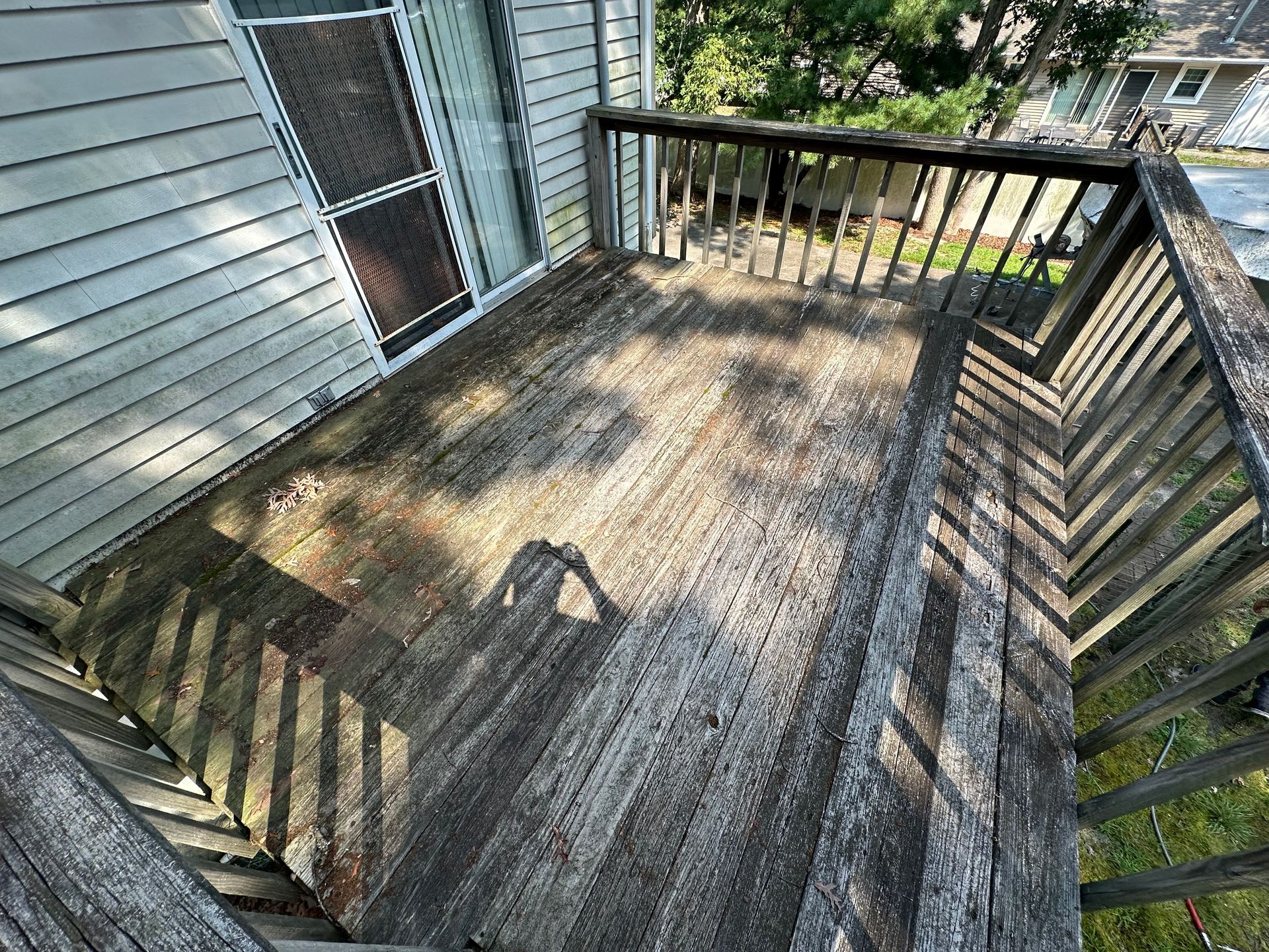 Weathered wooden deck beside a house, with railings casting shadows in sunlight.