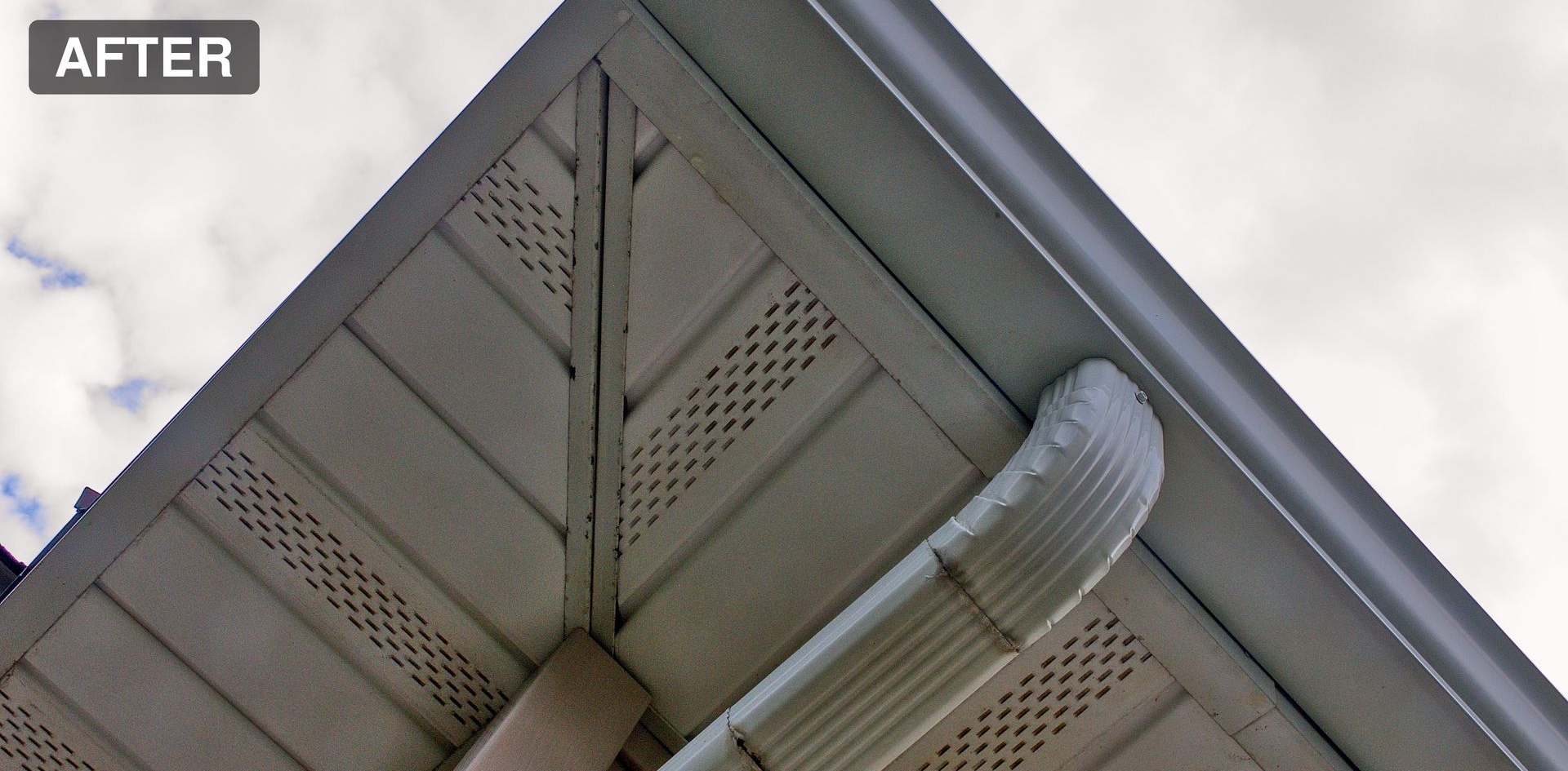 Soffit and roof eaves with white trim and a curved vent pipe against a cloudy sky