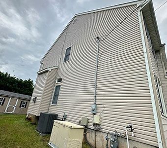 Side view of a beige house with utility meters, AC units, and siding along the foundation.
