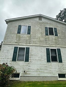 Two-story beige house with green shutters and several windows, viewed from outside