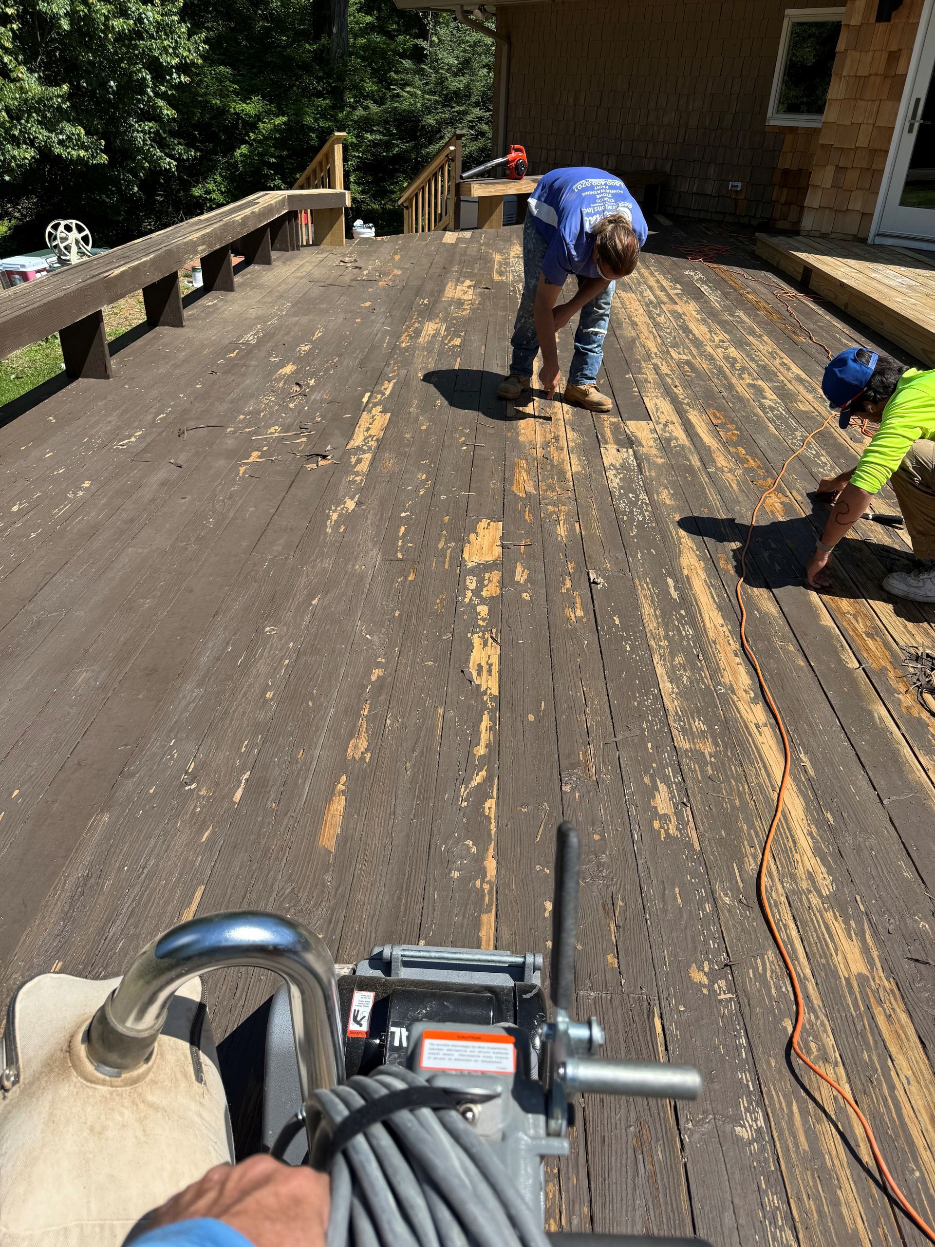 Weathered wooden deck beside a house, with railings casting shadows in sunlight.