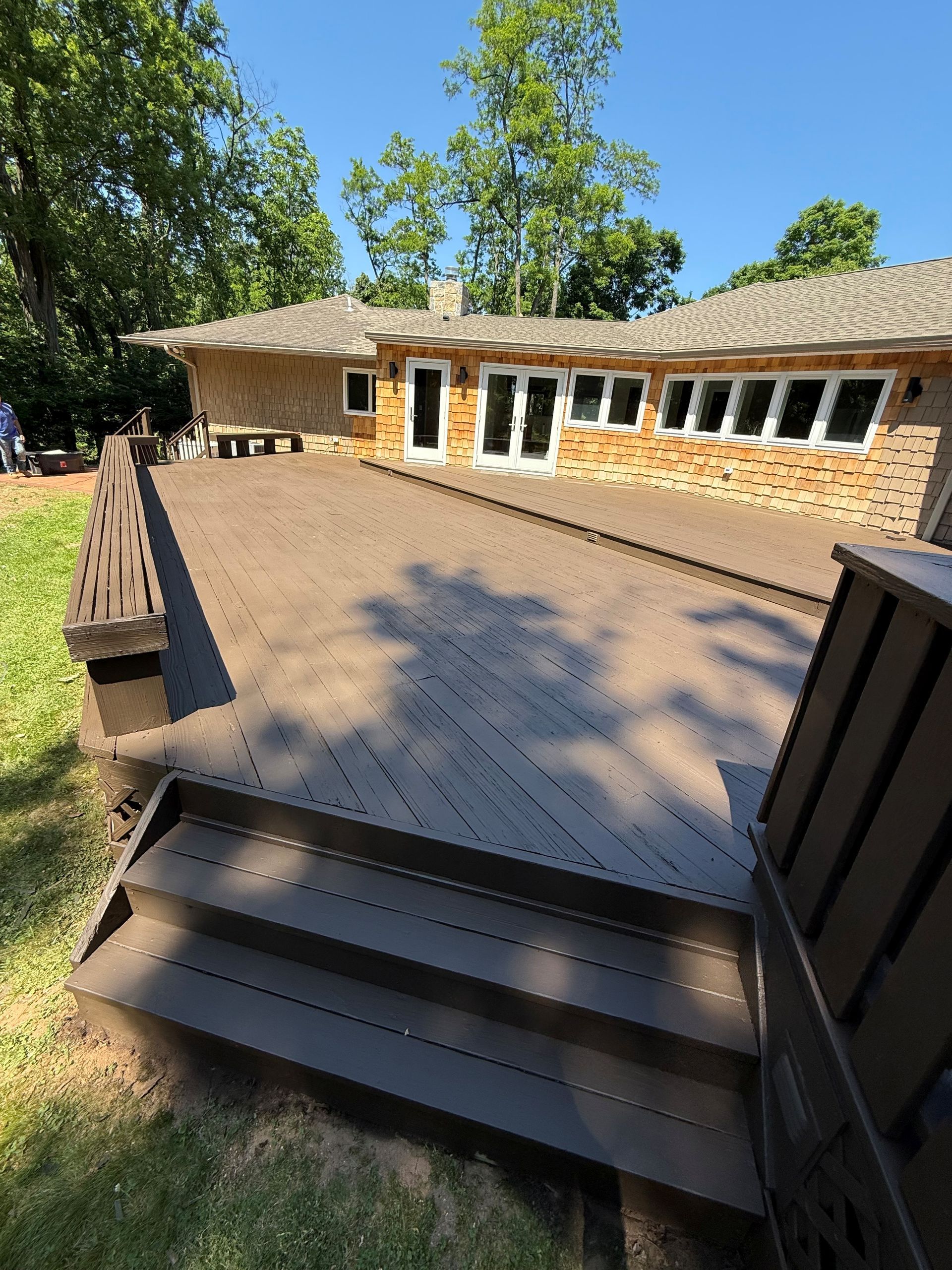 Weathered wooden deck beside a house, with brown railings and sunlight filtering through nearby trees