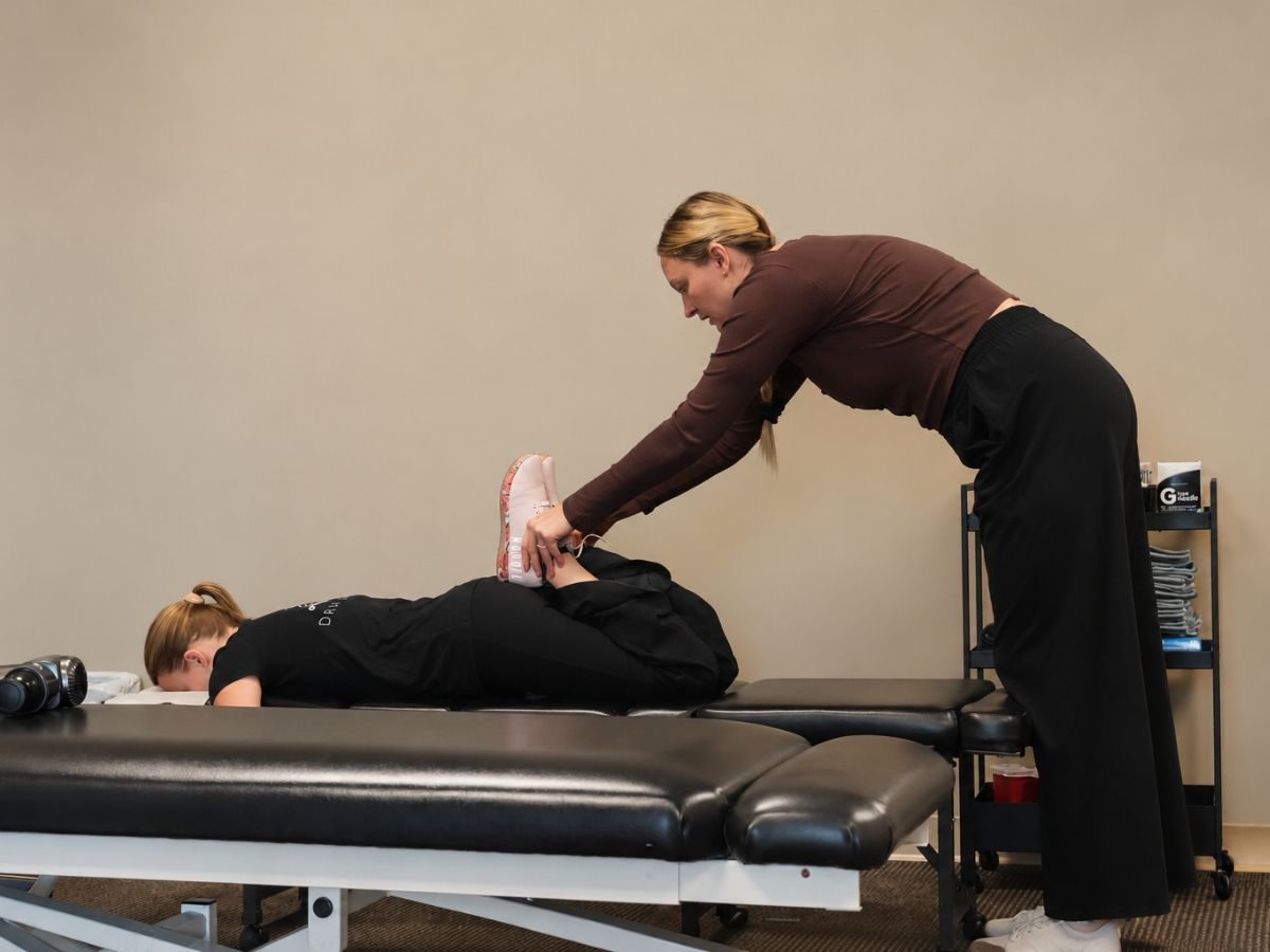 Chiropractor performing a prone knee and ankle mobility assessment on a female patient at Raise Chiropractic in Littleton, Colorado