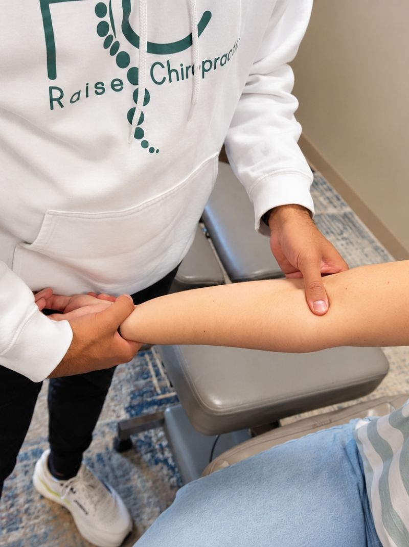 Dr. Neal assessing a female patient's extended arm for tennis elbow at Raise Chiropractic in Littleton, Colorado