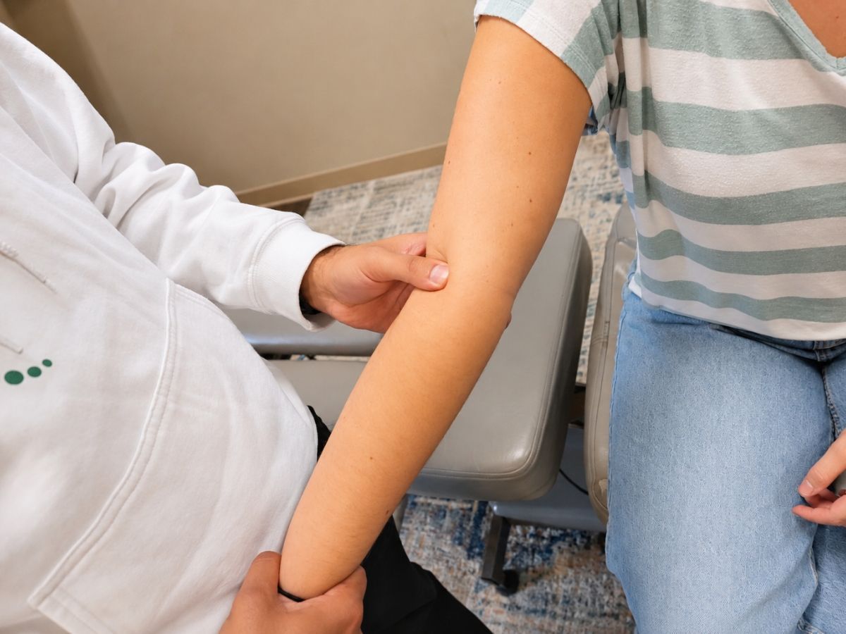 Dr. Neal examining a female patient's elbow and forearm at Raise Chiropractic in Littleton, Colorado