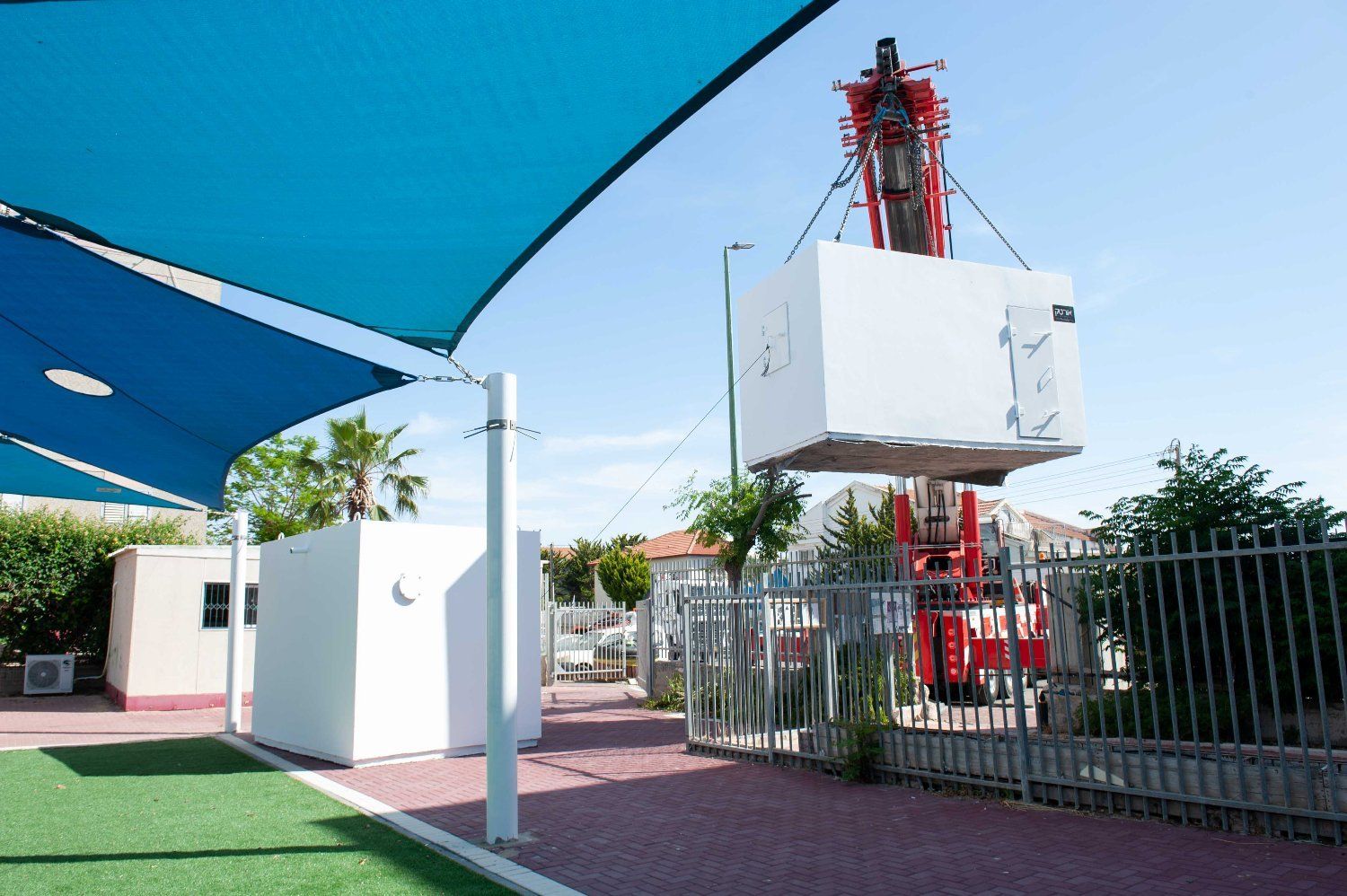 A red crane is lifting a large white box