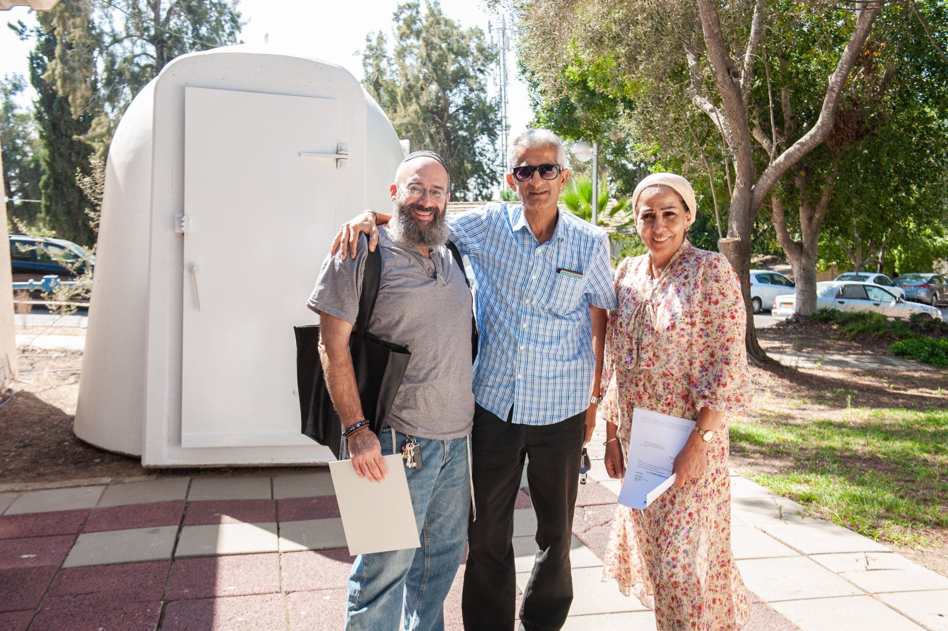 Three people are posing for a picture in front of a white building.