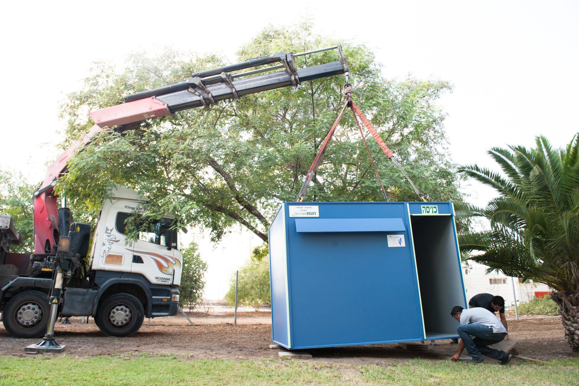 A crane is lifting a blue building into the air.