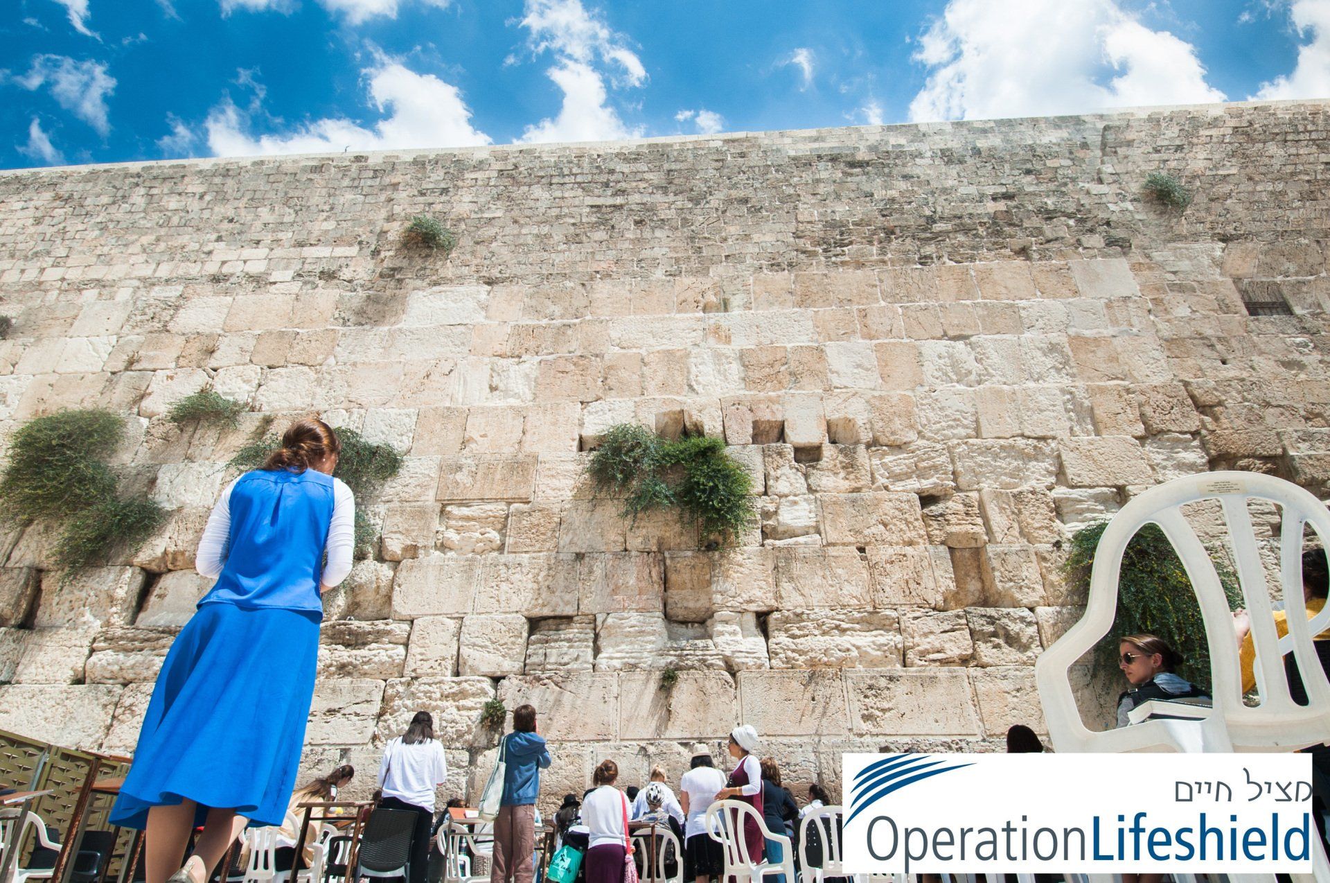 A woman in a blue skirt is praying at the western wall