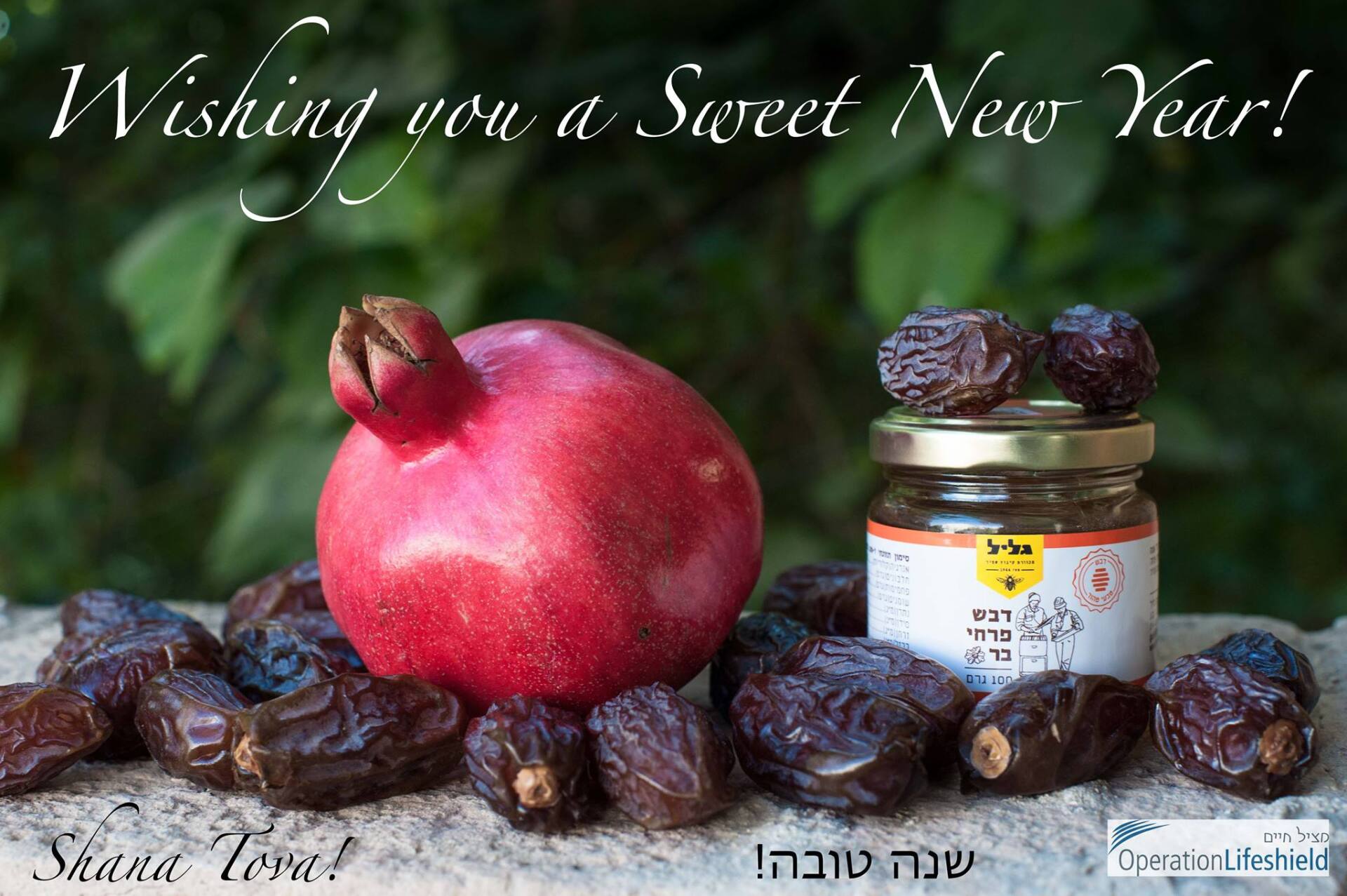 A pomegranate and dates are on a table with a jar of honey.