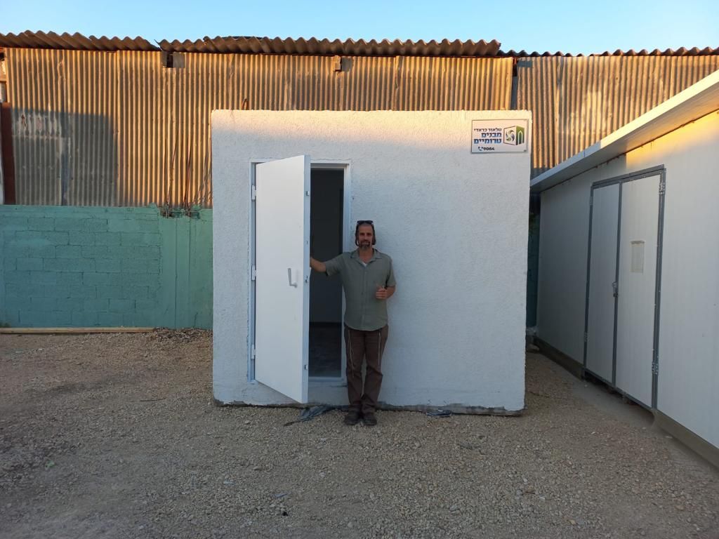 A man is standing in front of a small white shelter