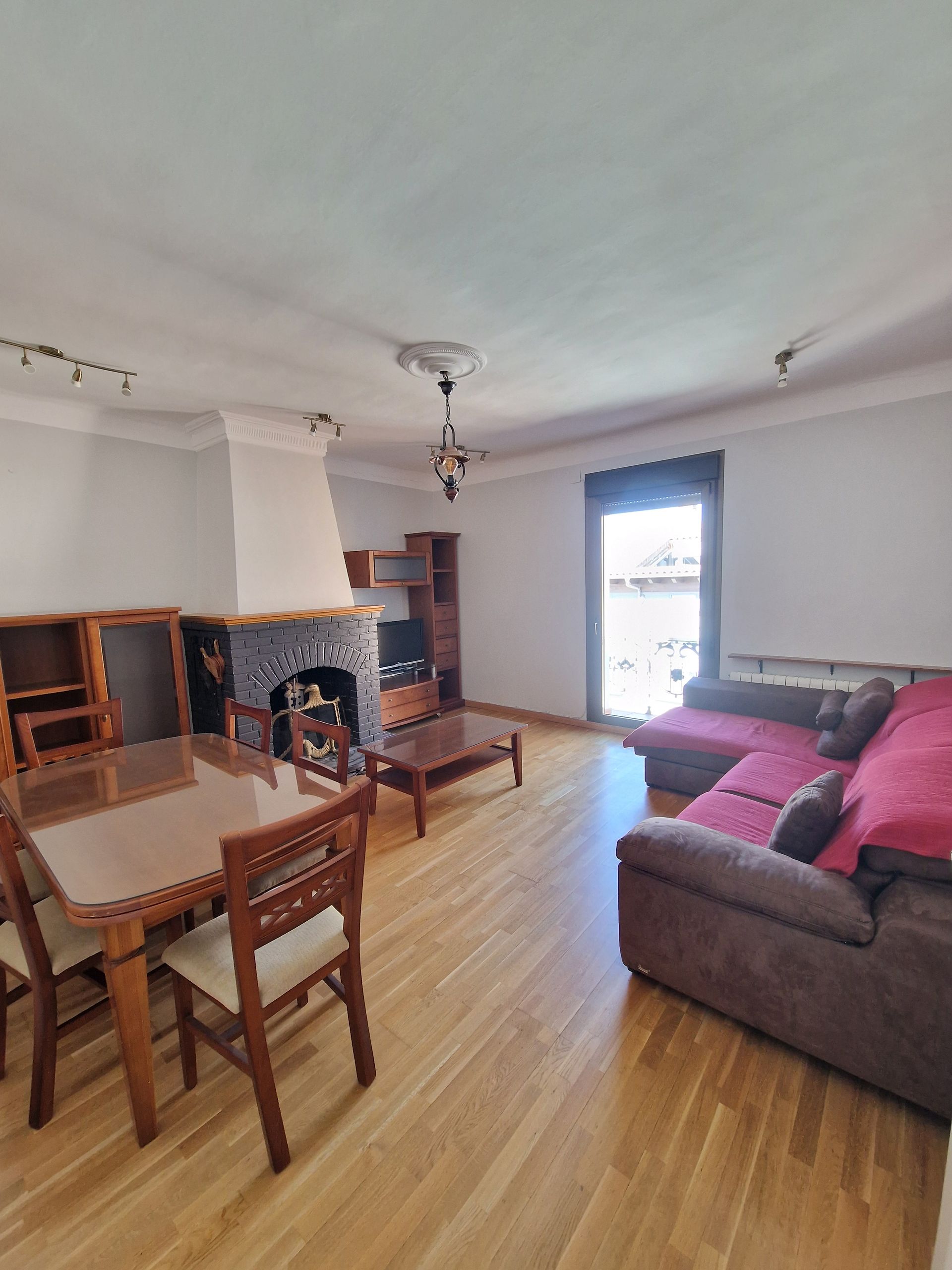 Sala de estar con sofá, mesa de comedor, chimenea y puerta abierta a un balcón luminoso.