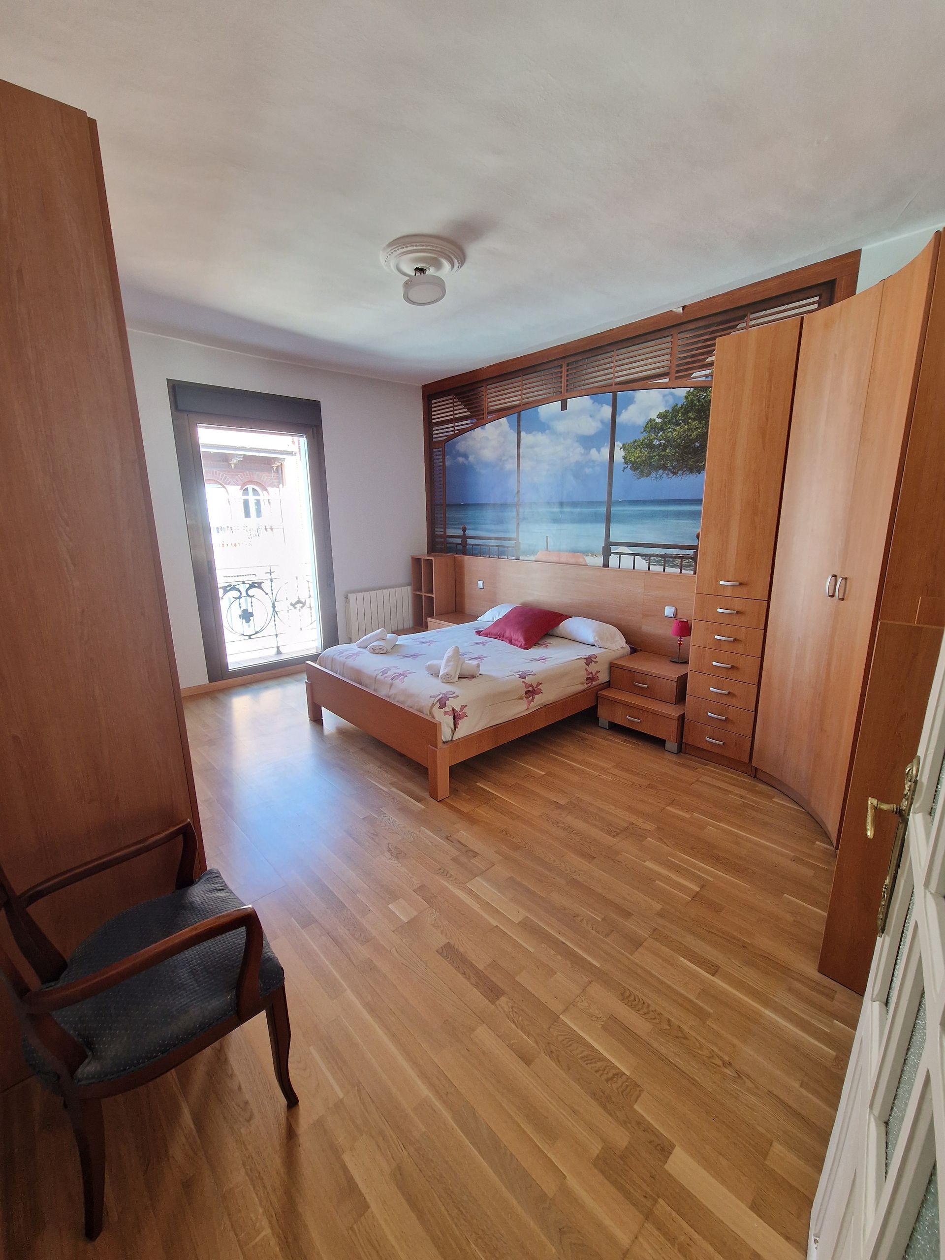 Habitación pequeña con cama individual, armario de madera, escritorio y puerta al balcón.