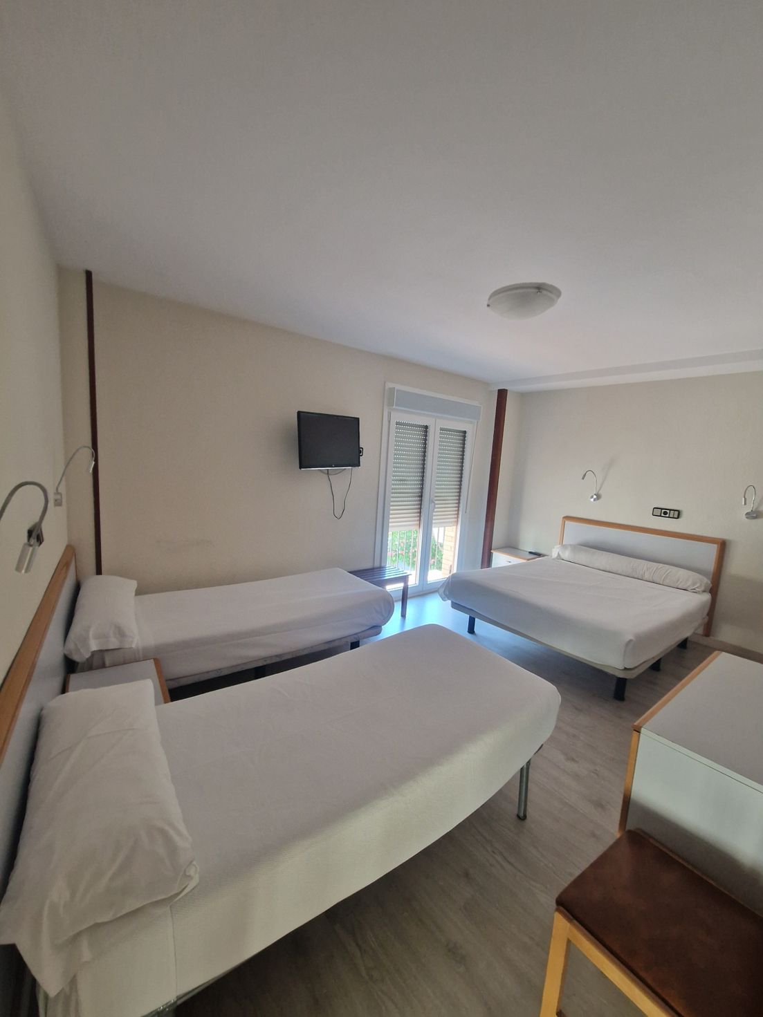 Habitación de hotel luminosa con cuatro camas individuales, televisor