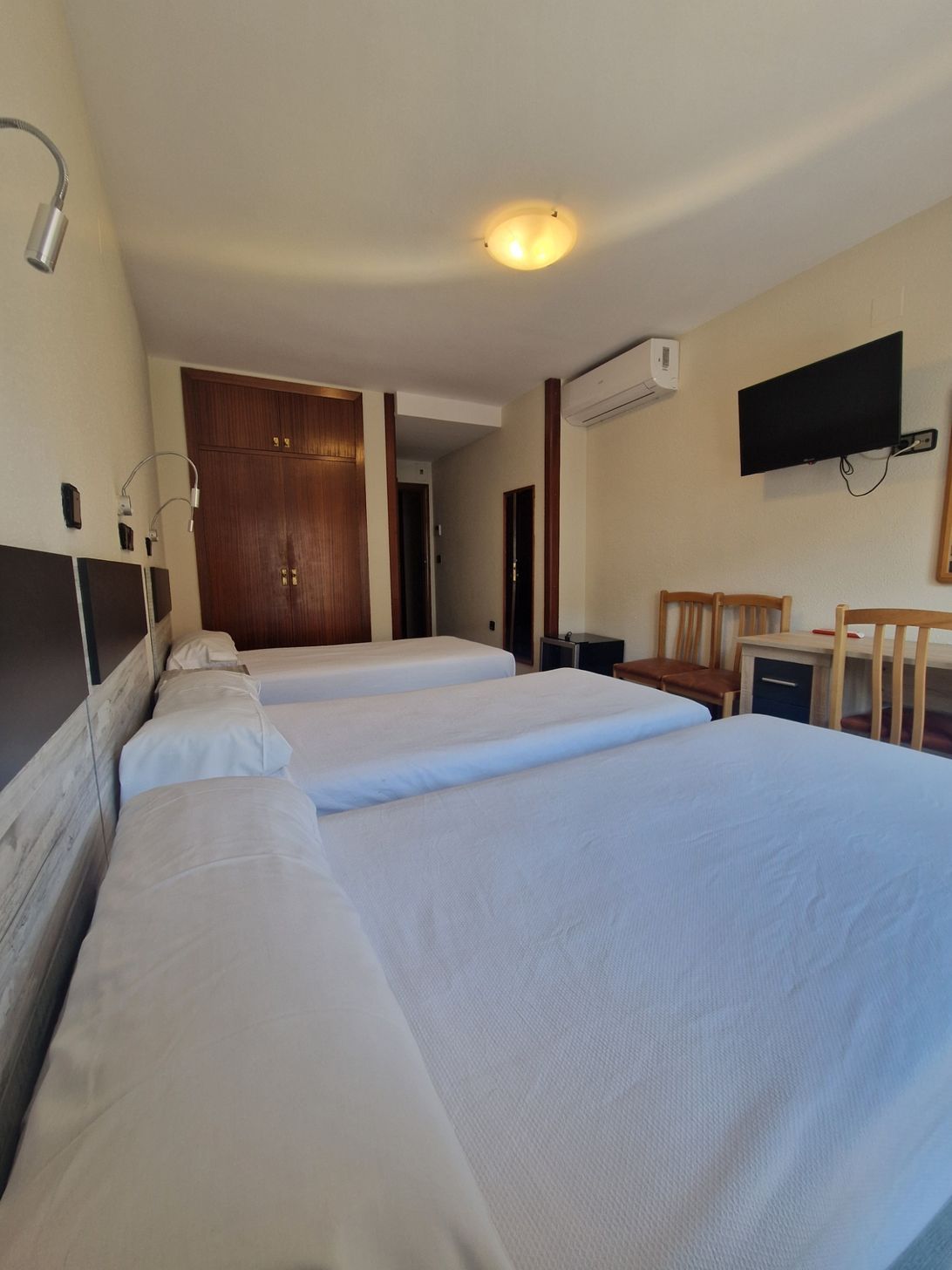 Habitación de hotel con dos camas individuales, televisor de pared, aire acondicionado y mesita junto a la ventana.