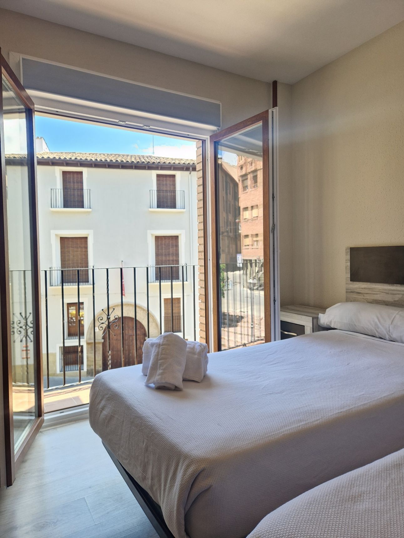Habitación luminosa con dos camas individuales y una puerta que da a un balcón con vistas a los edificios cercanos.