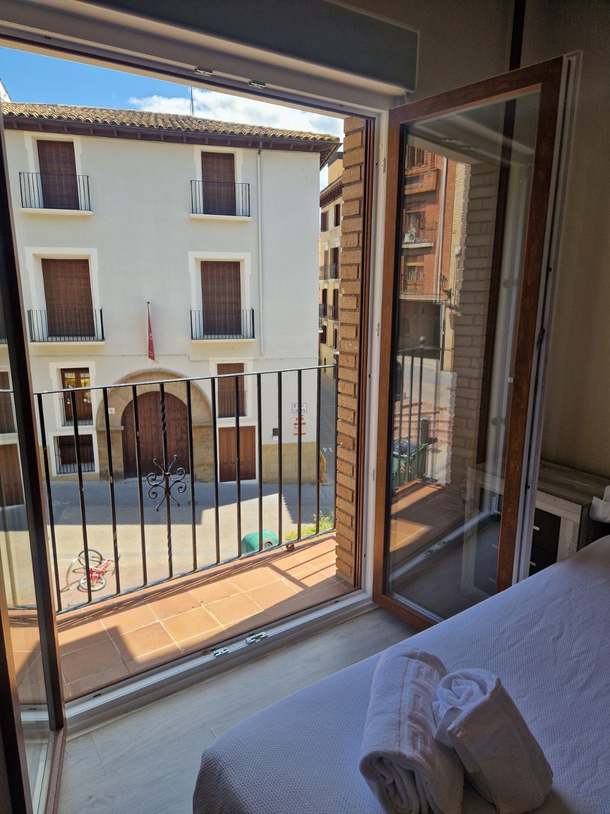 Ventana del dormitorio con vistas a un patio soleado con edificios vecinos y barandilla de balcón.