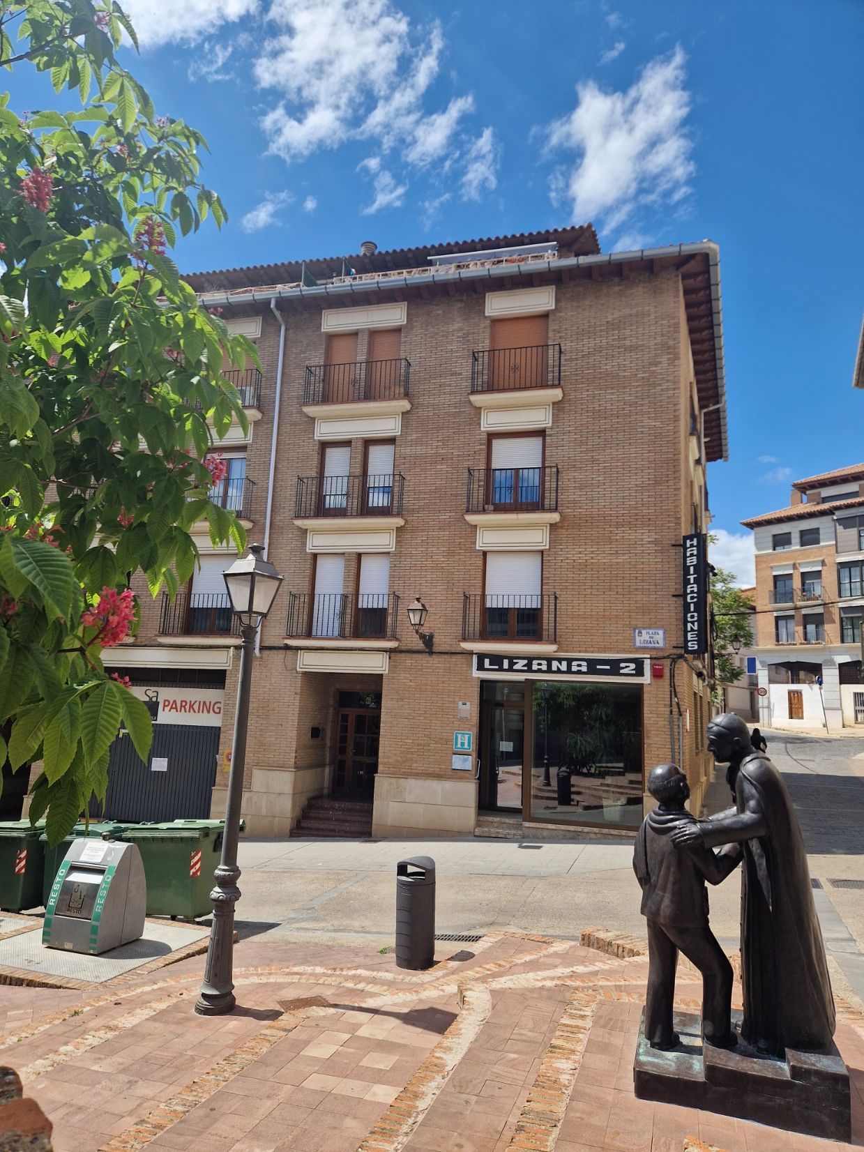 Edificio de apartamentos de ladrillo bañado por el sol, con balcones, escaparates y un cielo azul en una esquina.