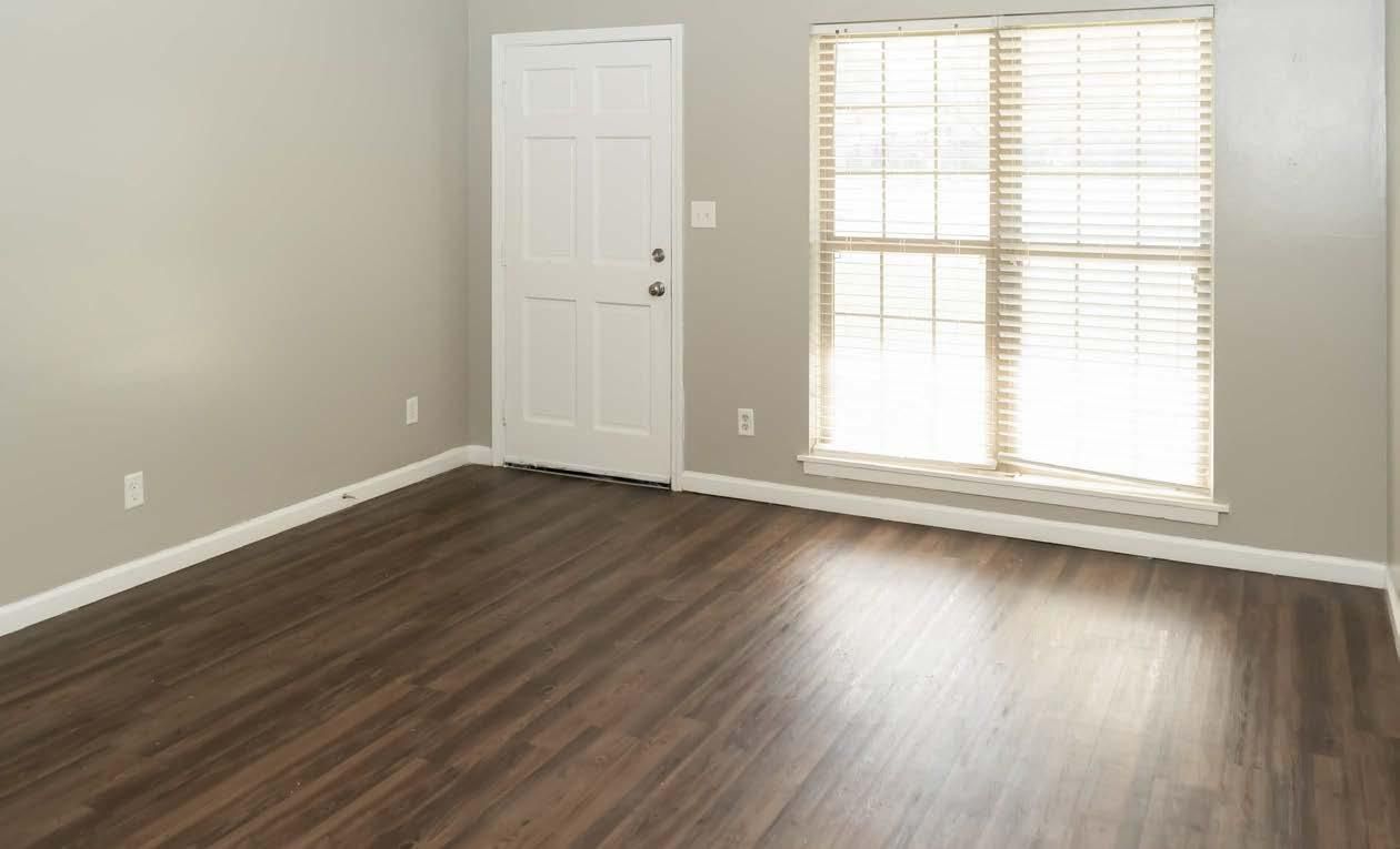 Empty room with dark wood flooring, gray walls, white door, and large window with blinds