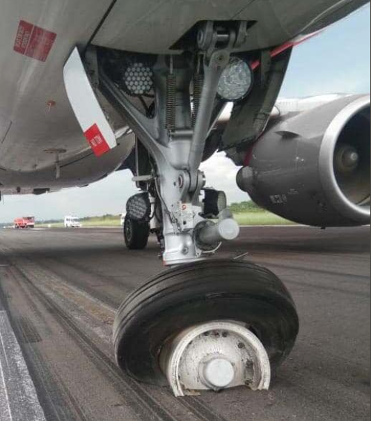 Aircraft nose landing gear with a flat tire on the runway.