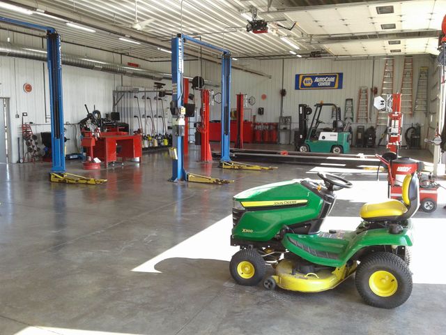 Auto repair shop with lifts and tools, and a green riding lawn mower in the foreground | Global Automotive