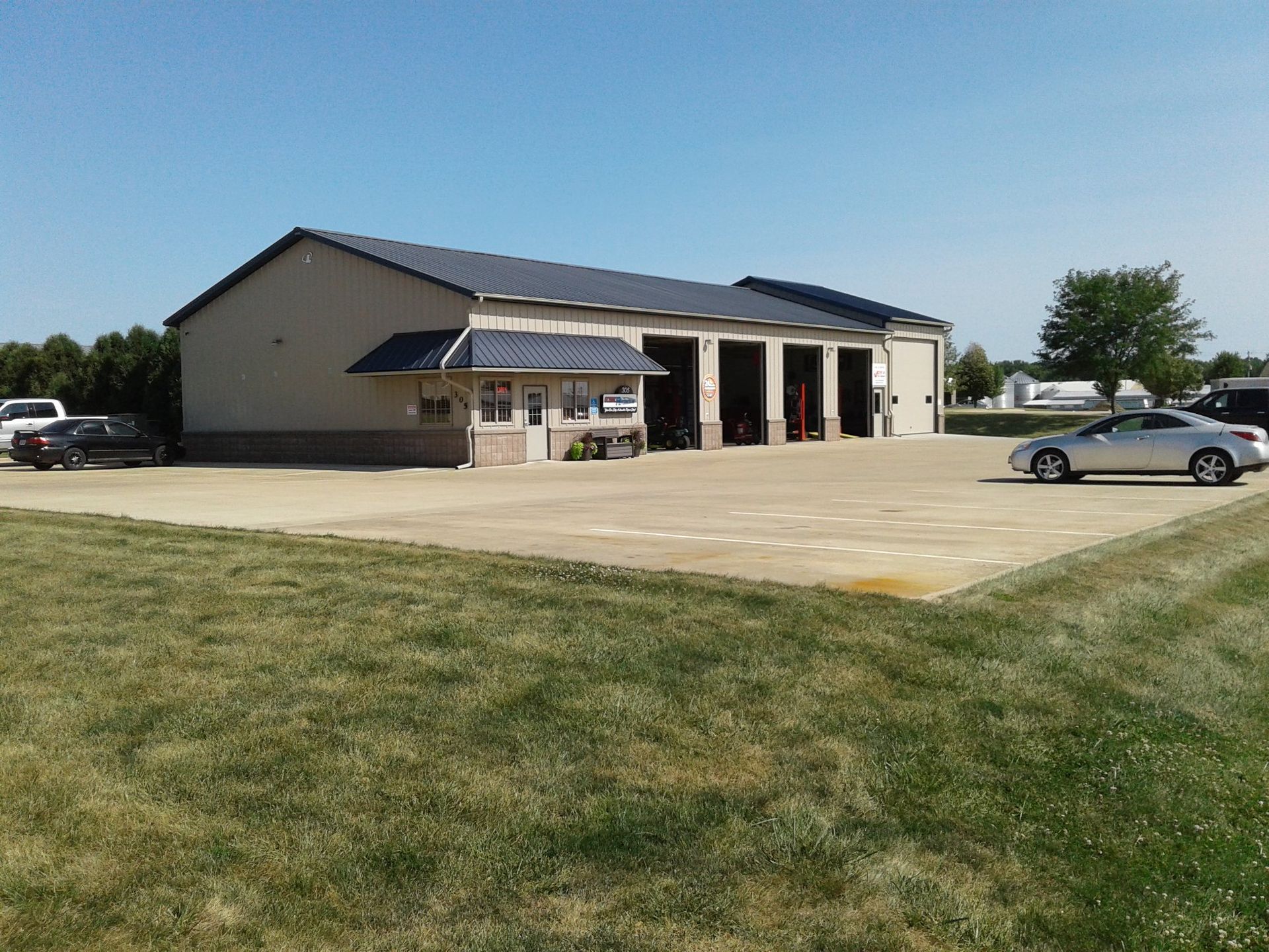 Small industrial building with open garage bays and parked cars on a sunny day | Global Automotive