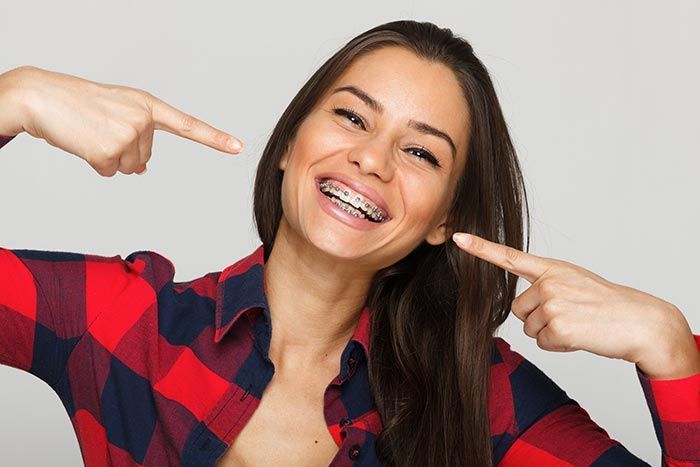 Una mujer que lleva aparato dental sonríe y señala sus dientes.